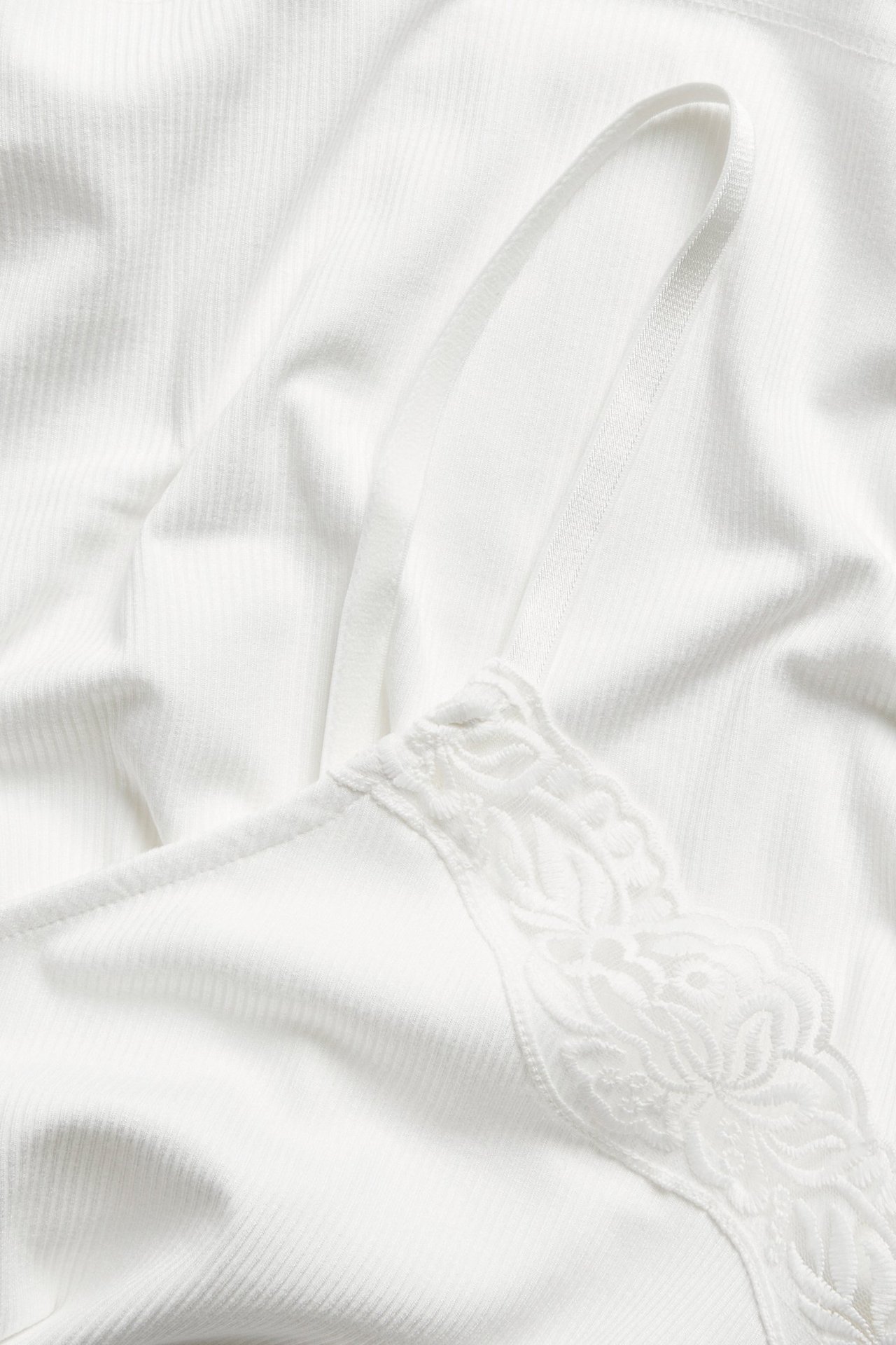 Närbild på ett offwhite ribbat linne med delikat spetskant vid halsringningen.
