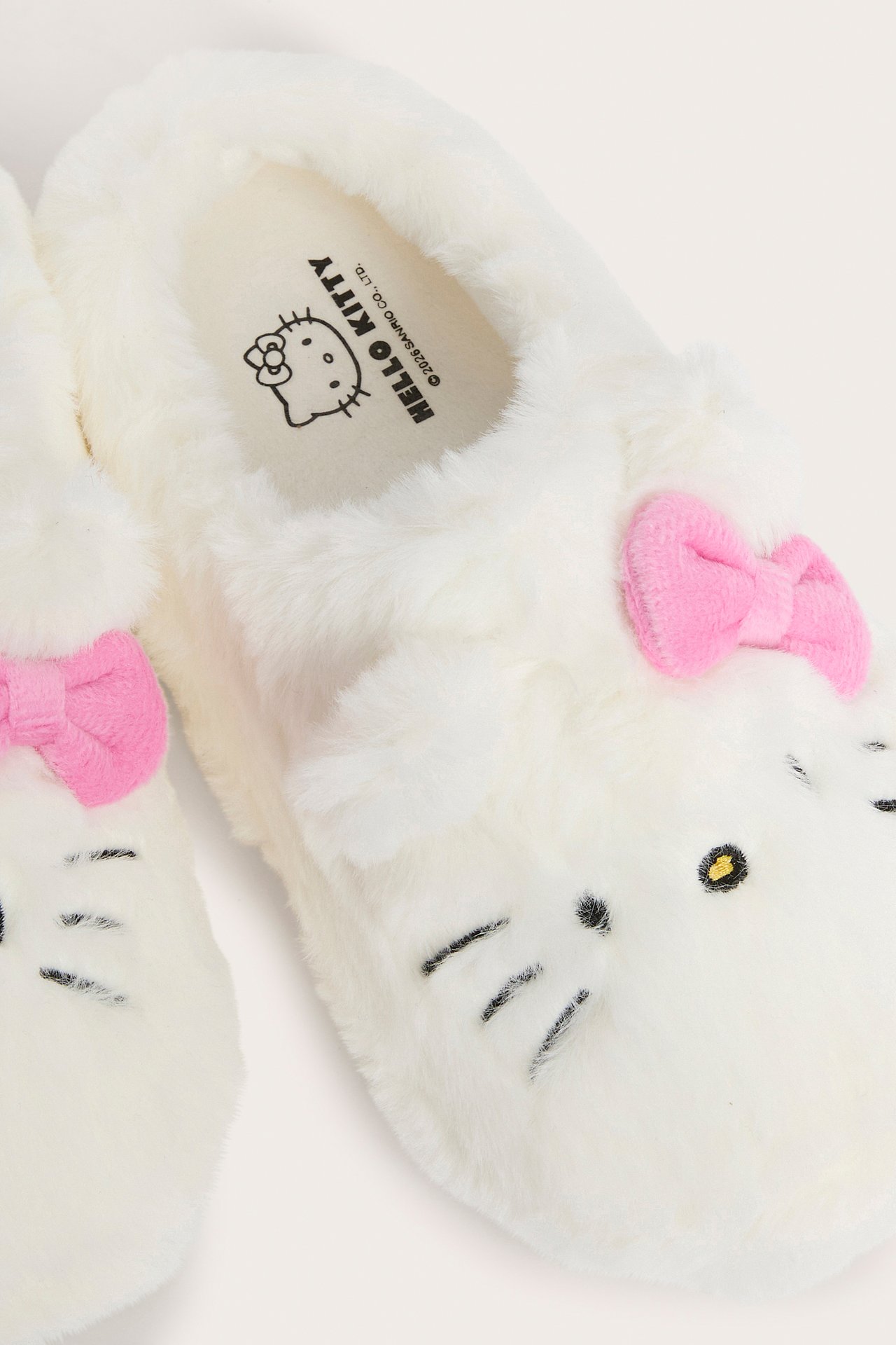 Lähikuva valkoisista pörröisistä Hello Kitty -tohveleista, joissa on vaaleanpunaiset rusetit ja brodeeratut kasvot.