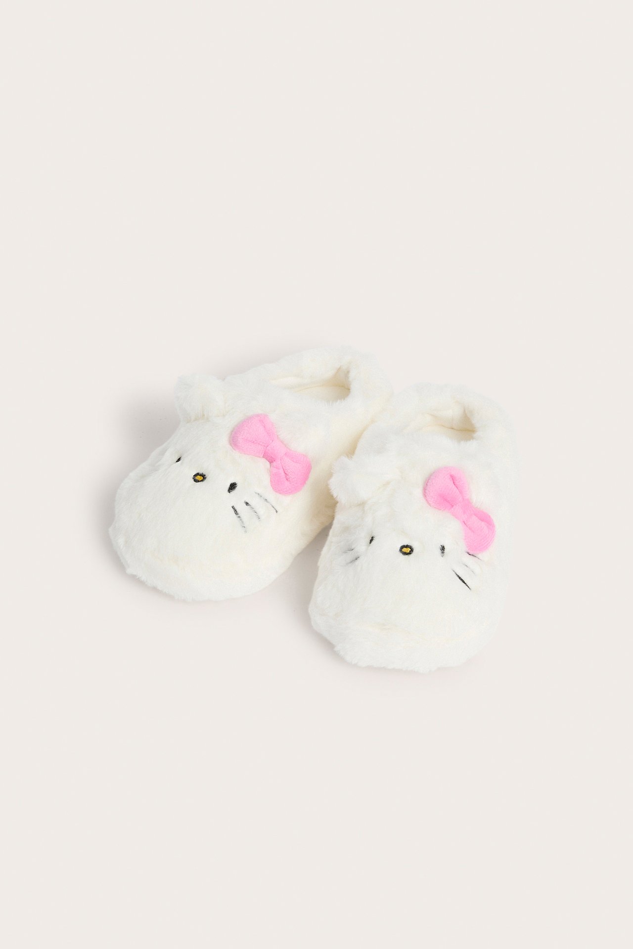 Pari valkoista pörröistä Hello Kitty -lasten tossua, joissa on vaaleanpunaiset rusetit, mustat silmät ja viikset.