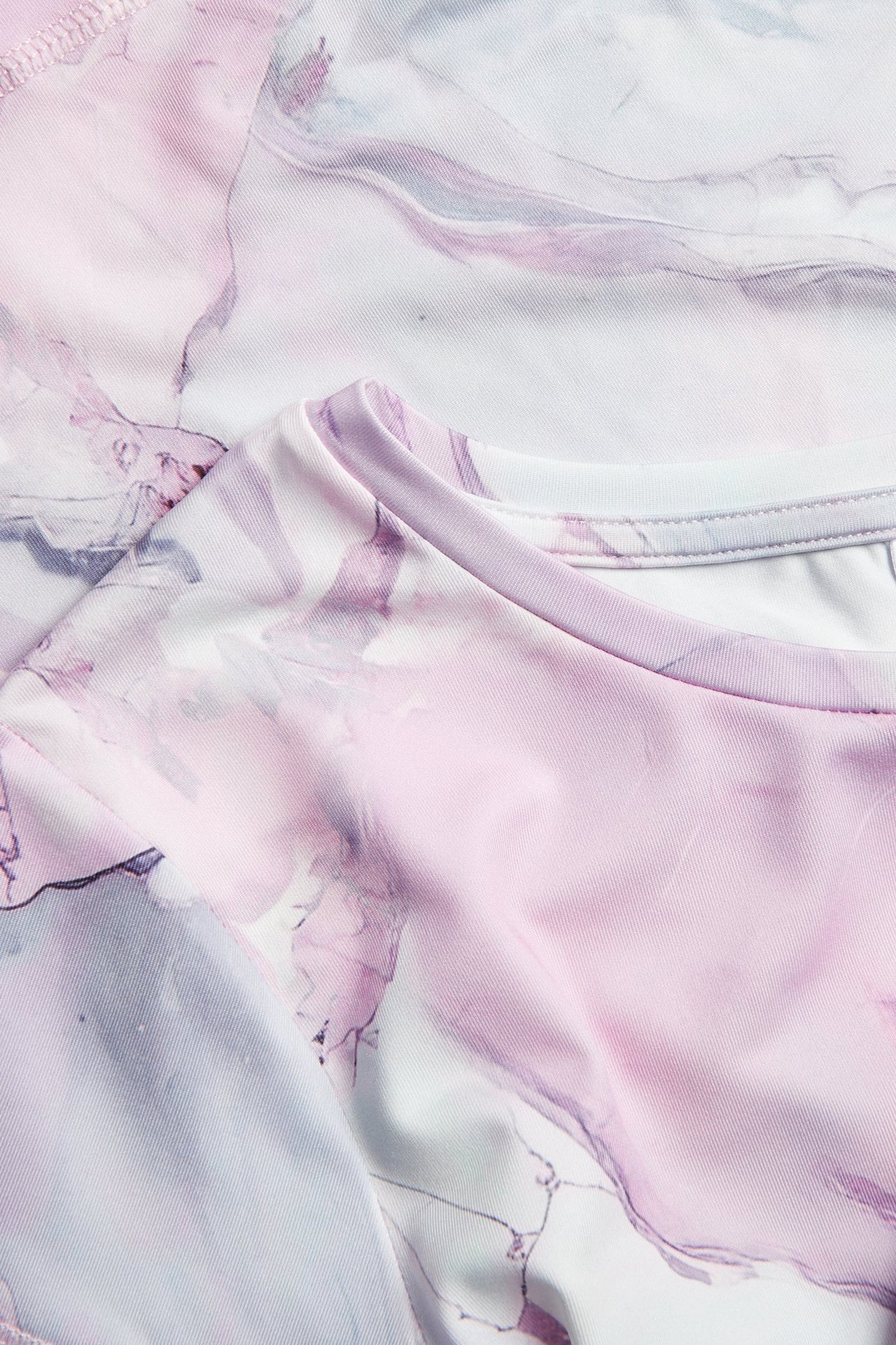 Zbliżenie na off-white, różowy i szary, marmurkowy top treningowy z dżerseju z okrągłym dekoltem.