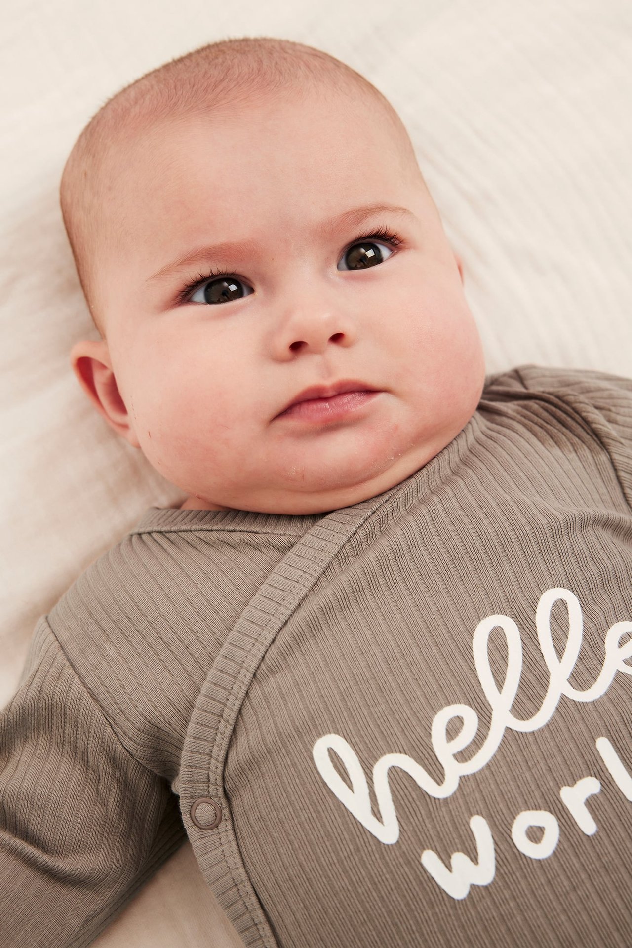 Lähikuva vauvasta harmaassa ribatussa pitkähihaisessa kietaisubodyssä, jossa teksti "hello world".
