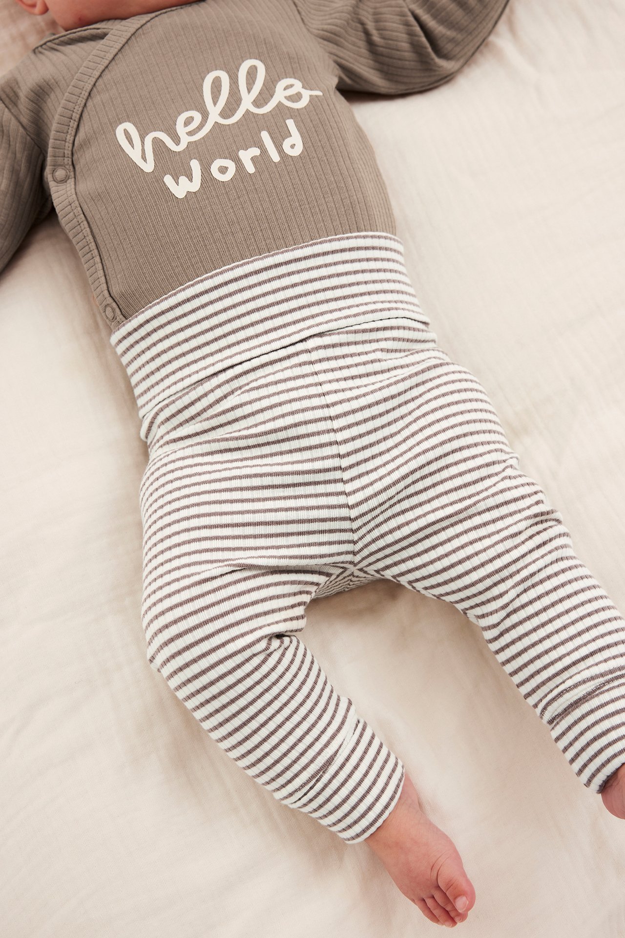 Ovanifrån vy av baby i randiga ribbade byxor och grå ribbad 'hello world' body.