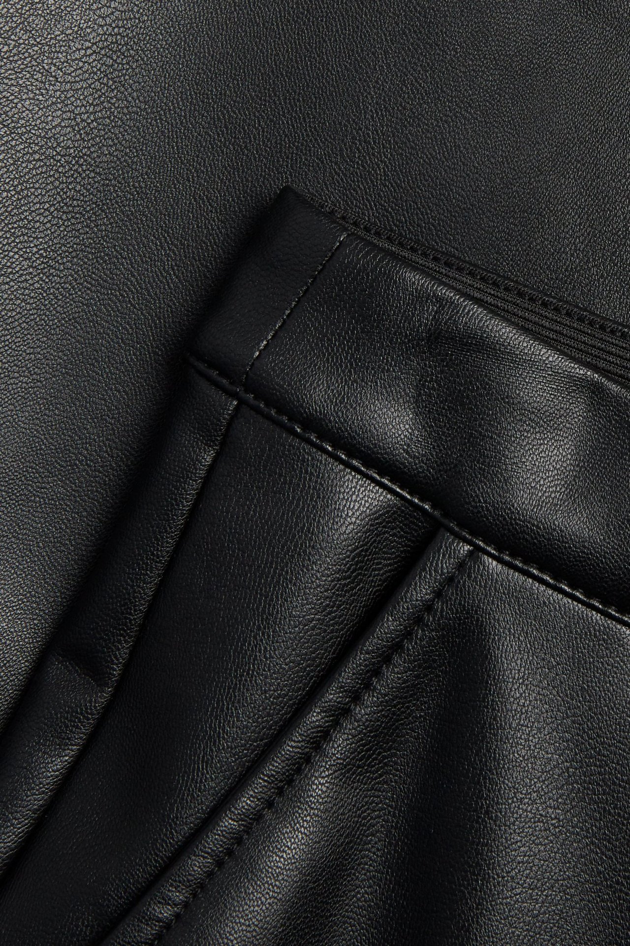 Nærbilde av et svart utsvunget langt skjørt i imitert skinn, viser tekstur, lomme og elastisk midjebånd.