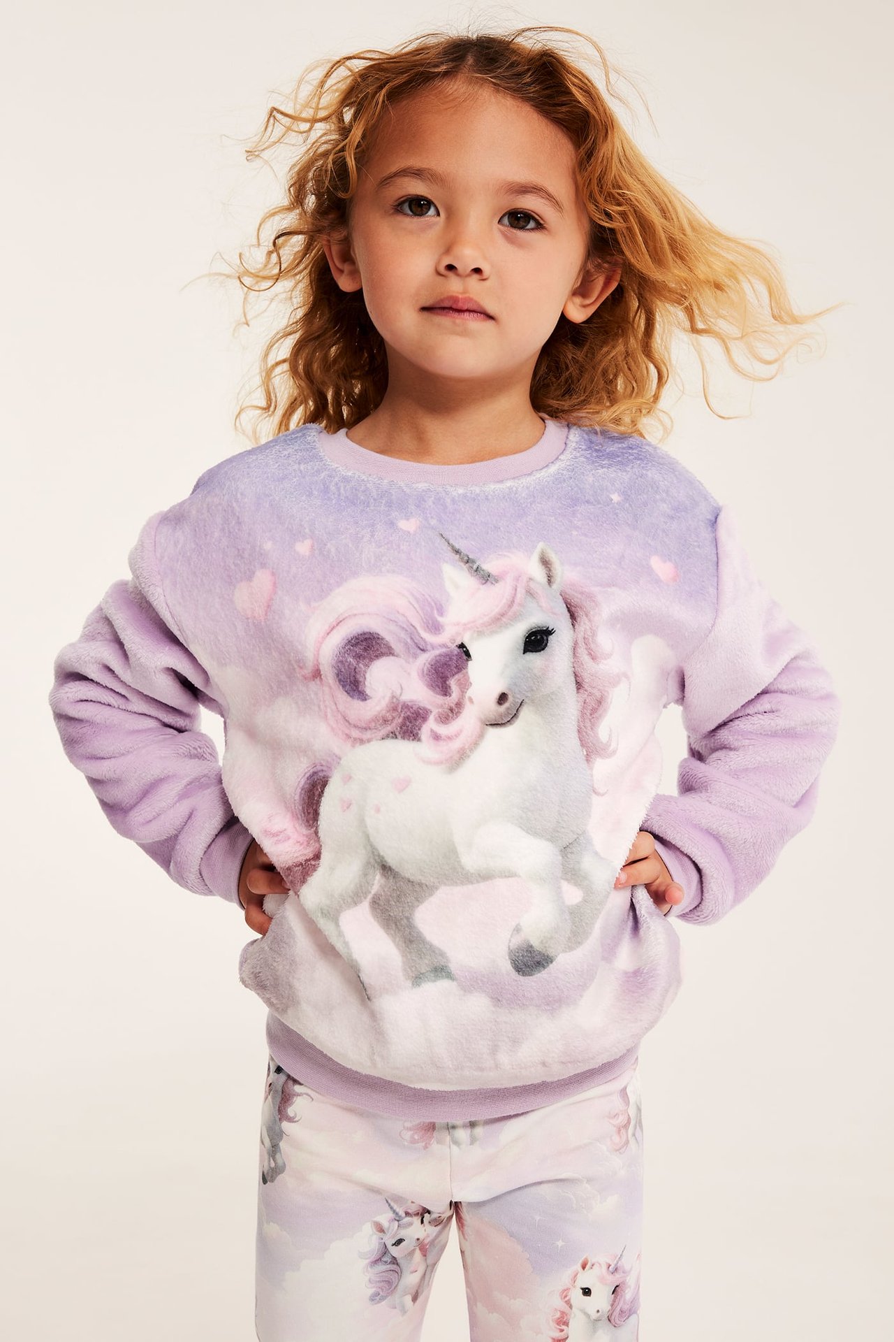 Front: barn i lilla enhjørningmønstret plysjgenser og matchende mønstrede leggings.