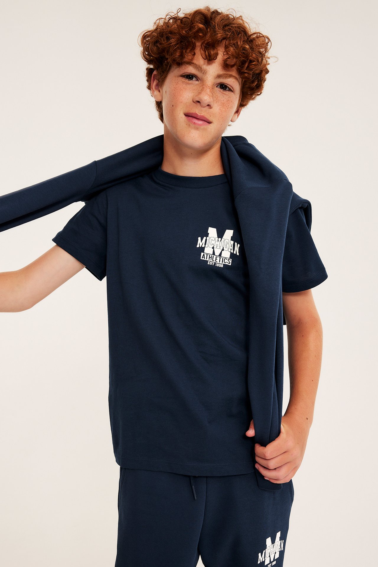 Widok z przodu dziecka w granatowym T-shircie z białym nadrukiem Michigan, do tego pasujące spodnie dresowe i bluza.