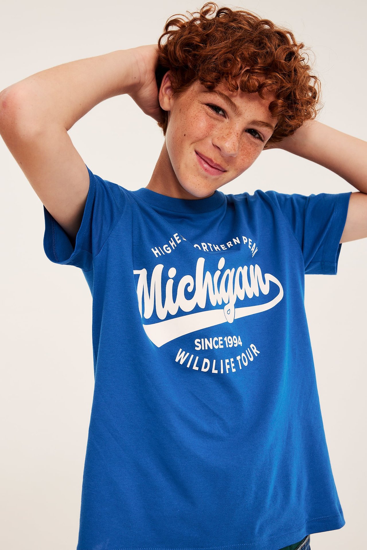 Widok z przodu dziecka w niebieskim t-shircie z białym nadrukiem 'Michigan Wildlife Tour since 1994'.