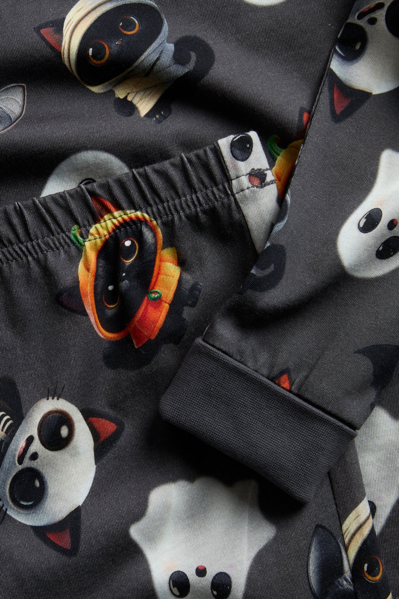 Närbild av mörkgrå pyjamas med Halloween-katt och spöktryck, med resår i midjan och ribbad mudd.