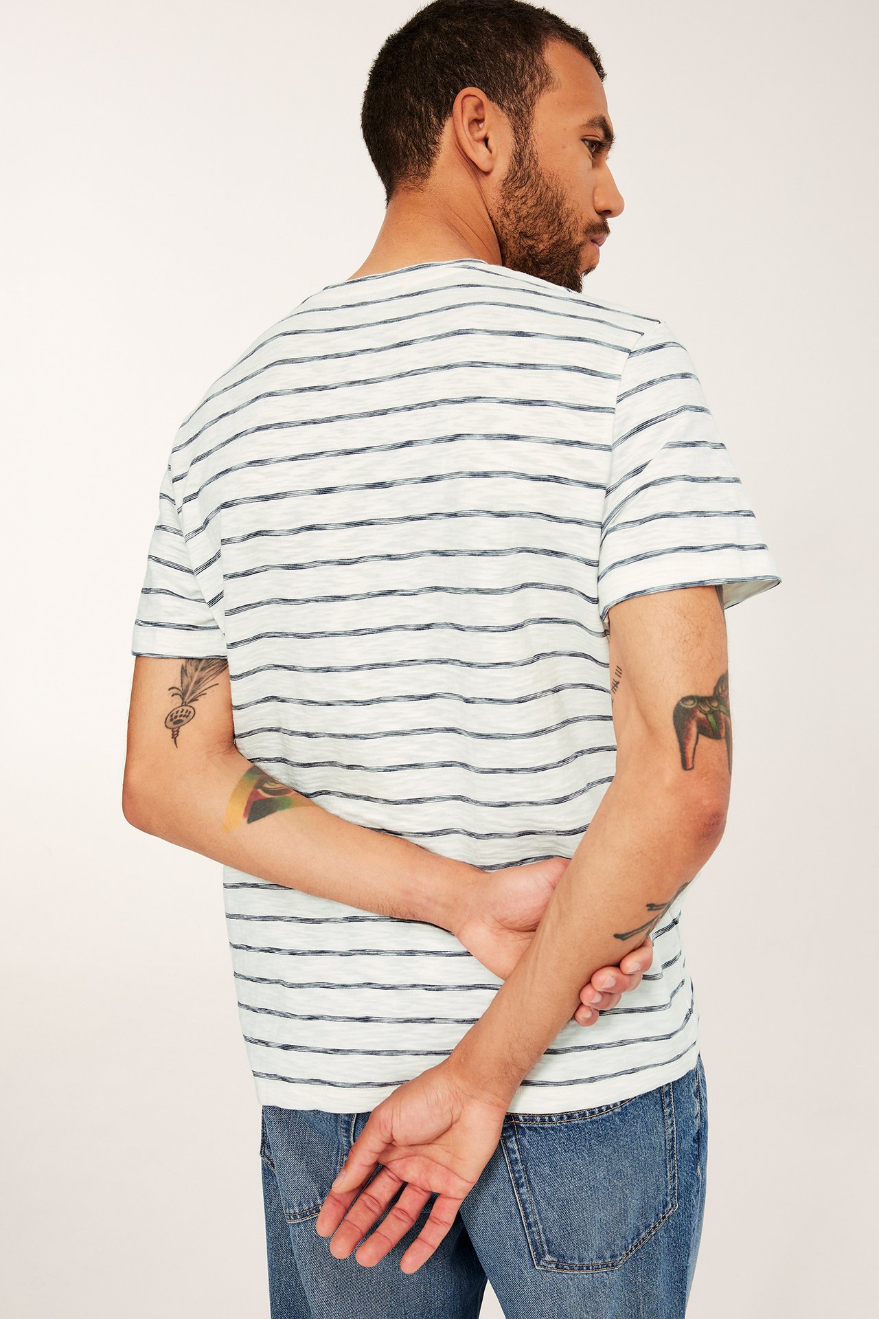 Bakfra: mann i lys grå slub-bomulls-t-skjorte med mørkeblå striper og blå jeans.