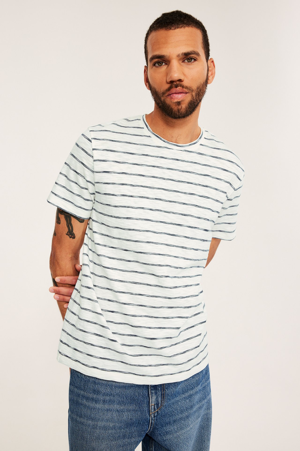 Forfra, mann i lys blå bomulls-t-skjorte med mørkeblå striper og blå jeans.