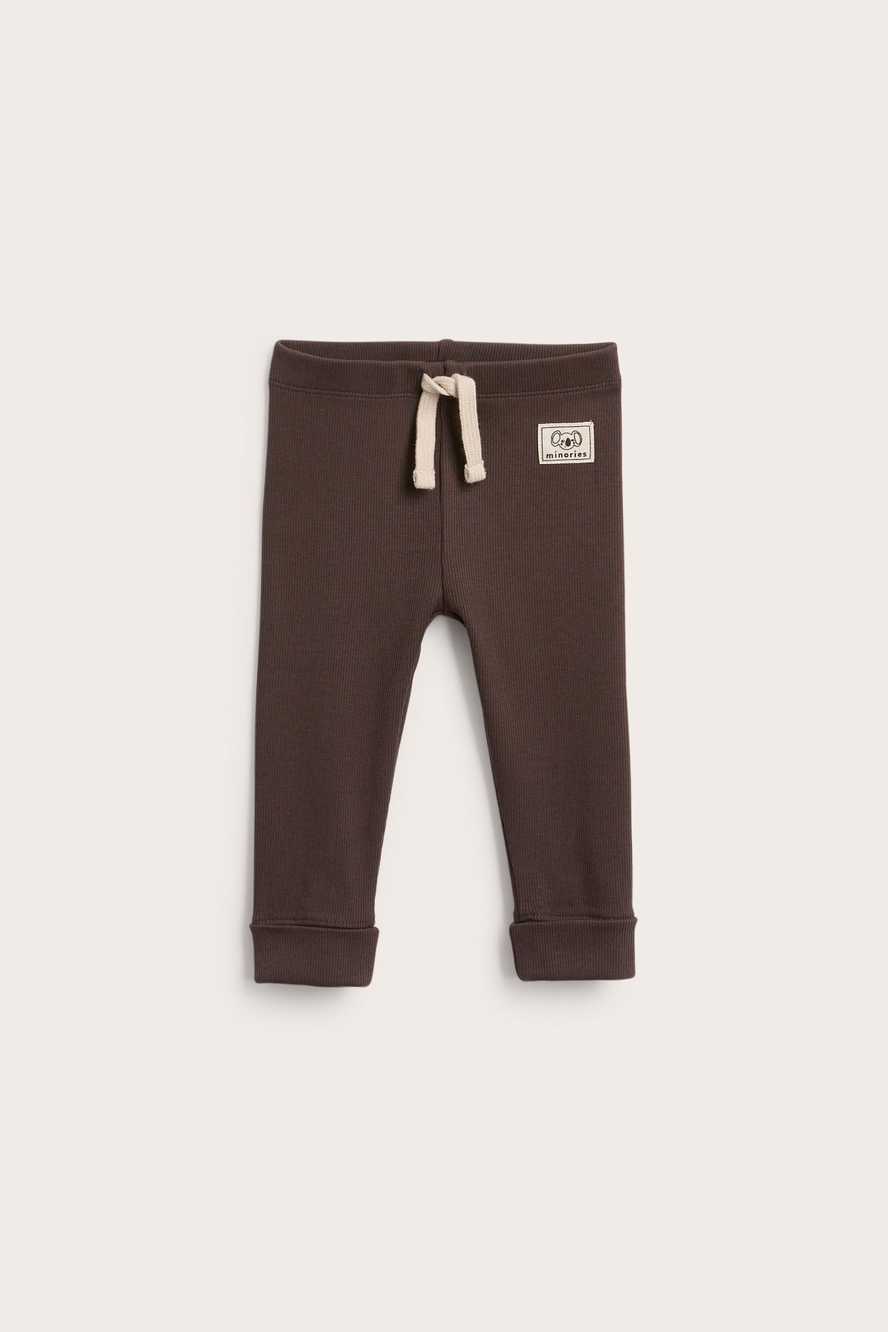 Frontbilde av baby mørkebrune ribbestrikkede leggings med snor og etikett.