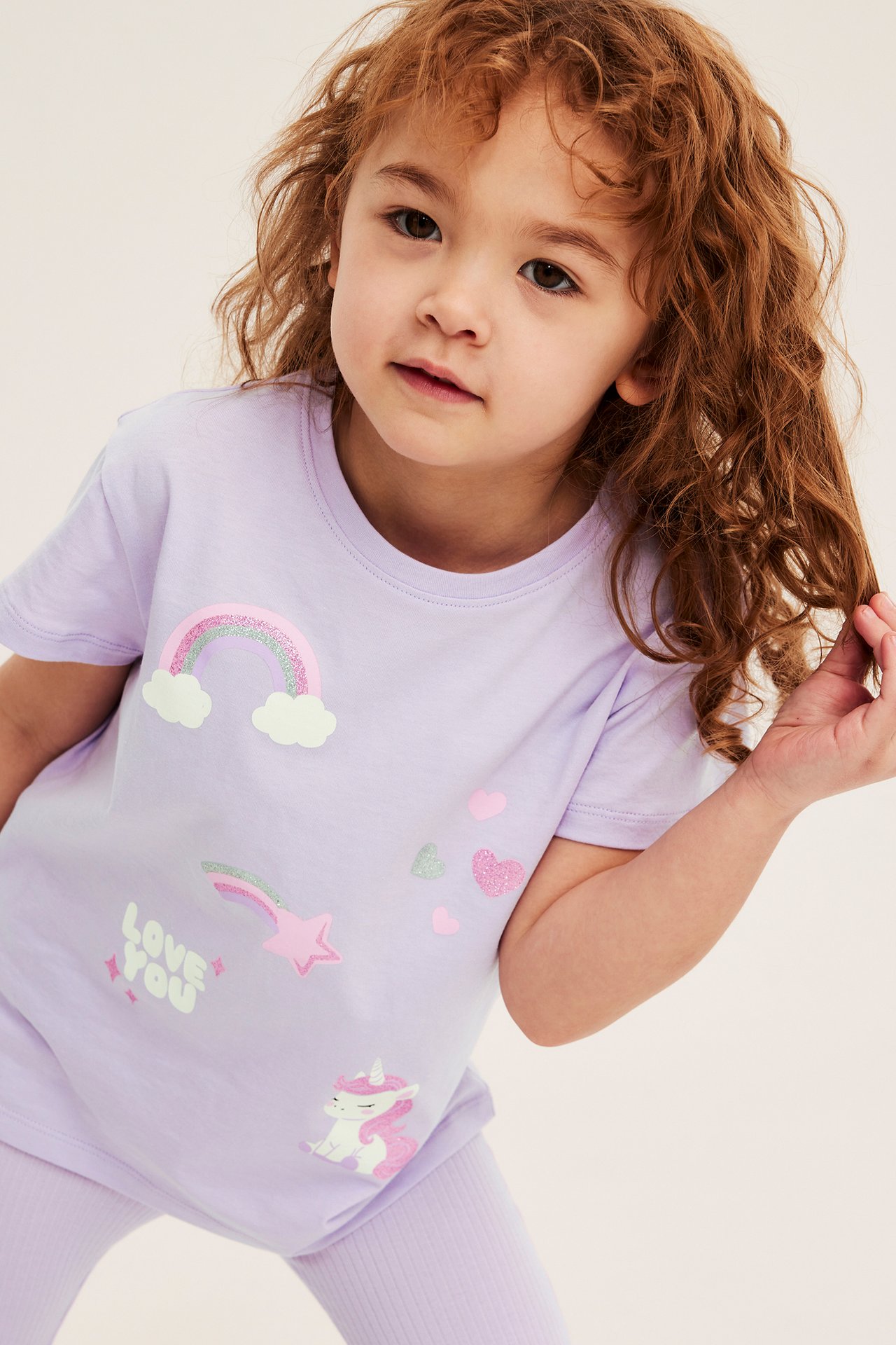 Frontvy: Barn i ljuslila bomullstopp med enhörning, regnbåge och hjärtan, matchande leggings.