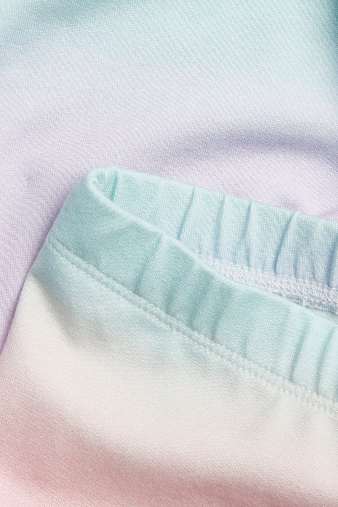 Zbliżenie na dziecięce legginsy z bawełnianej dzianiny z tęczowym wzorem i jasnoniebieskim elastycznym pasem.