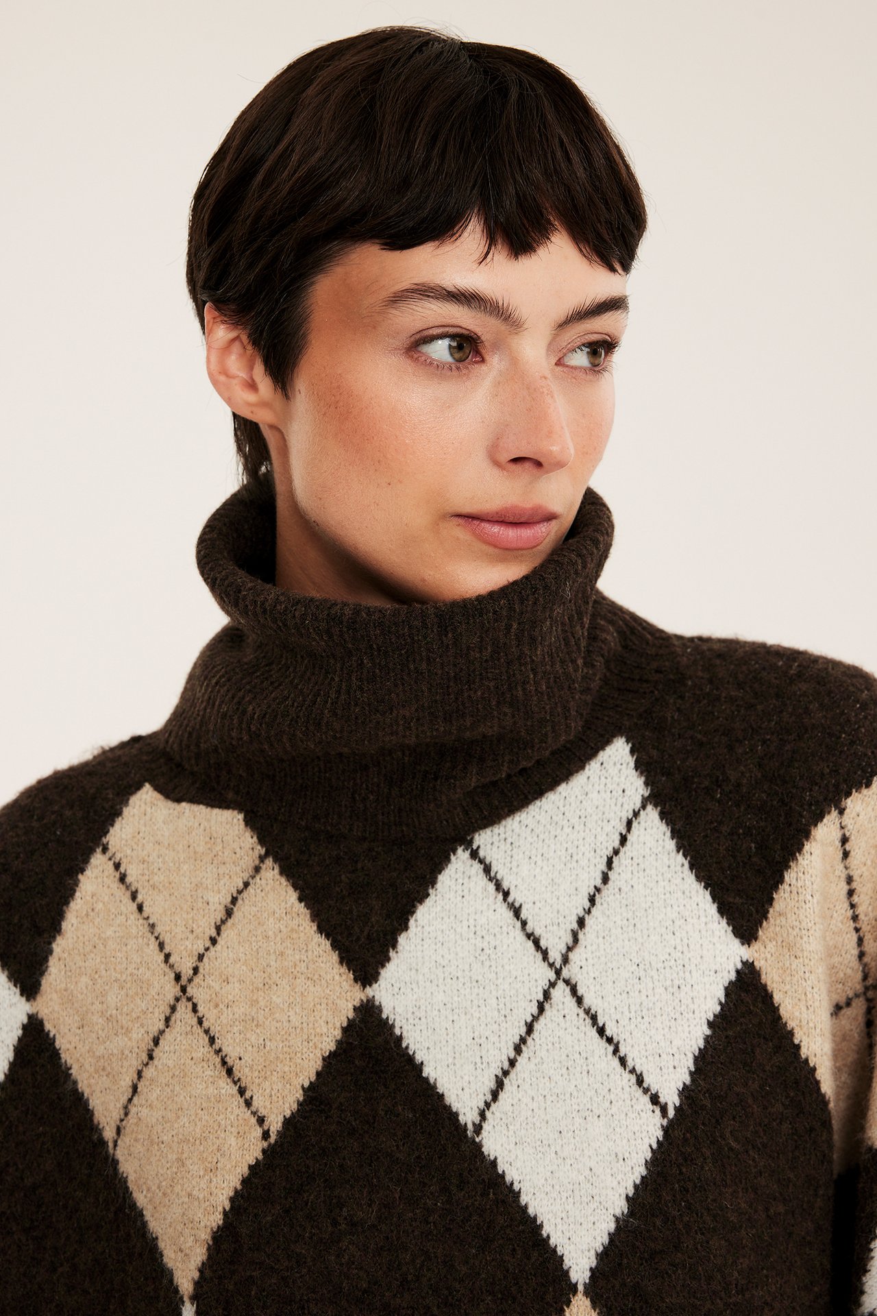 Lähikuva naismallista yllään ruskea, beige ja valkoinen argyle-poolopaita.