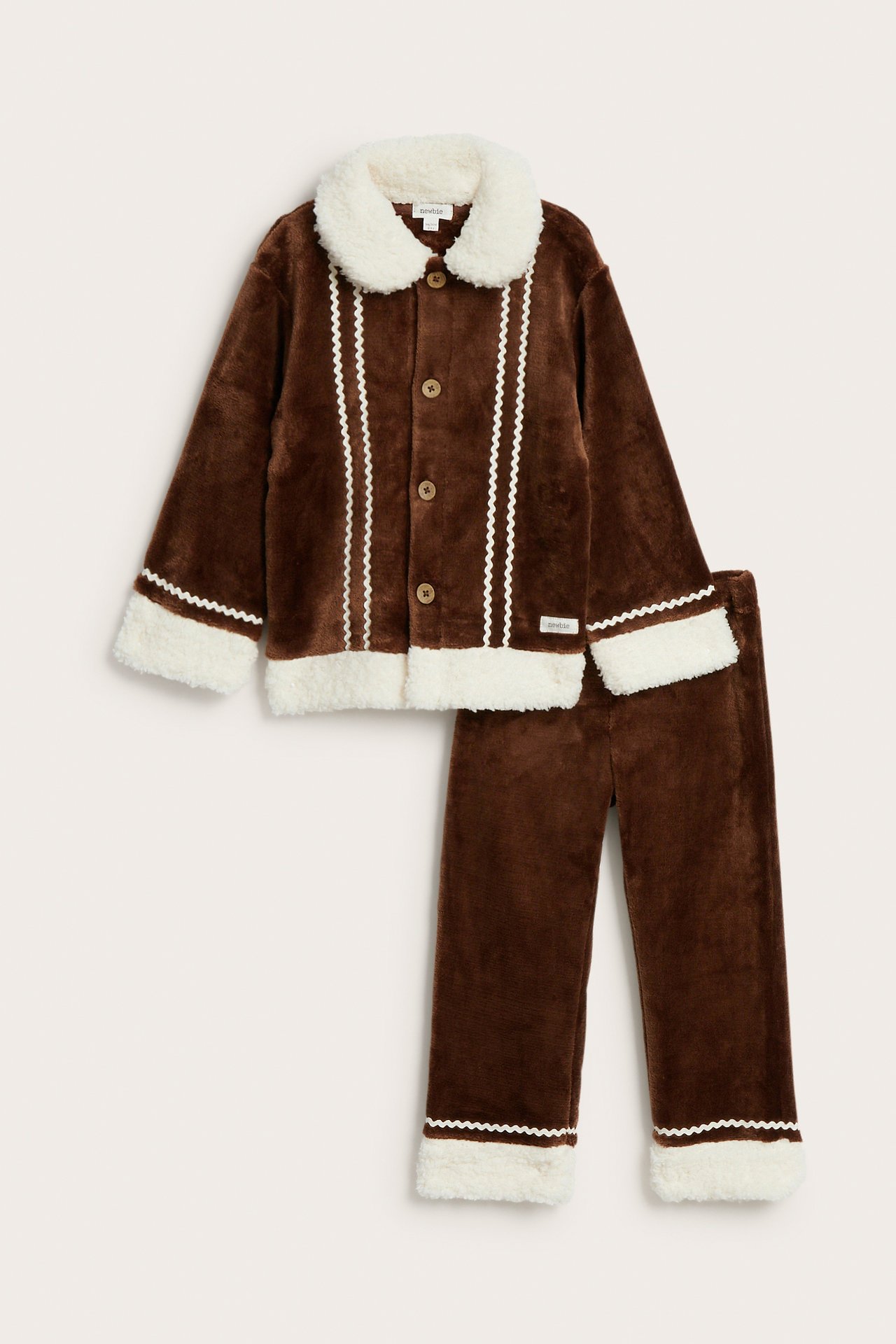 Framifrån, brunt plysch pyjamasset för barn med vit fuskpäls och sicksackdetaljer.