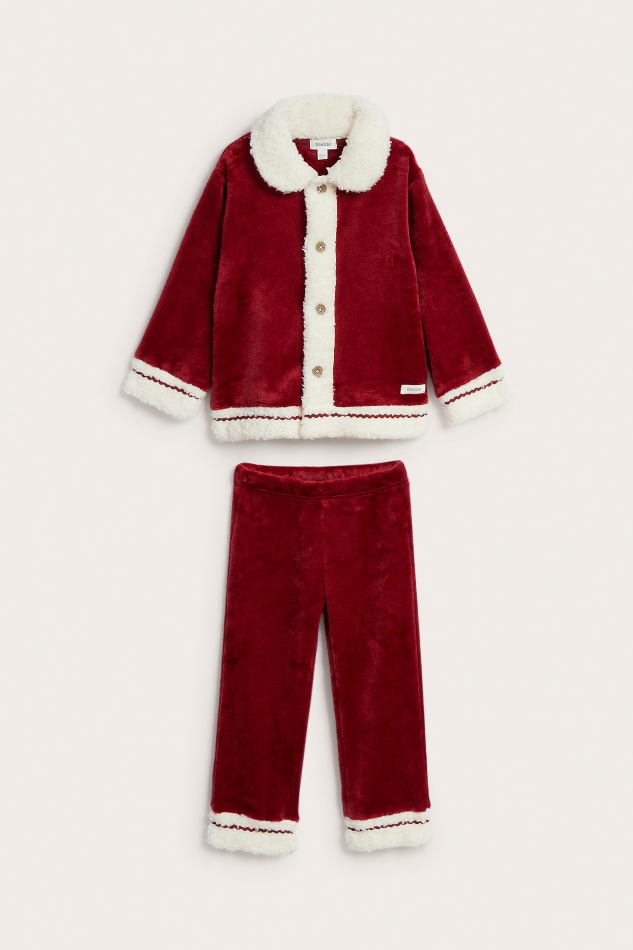 Frontvisning av et barnes rødt todelt pyjamassett i plysj med hvit fuskepels og knapper.