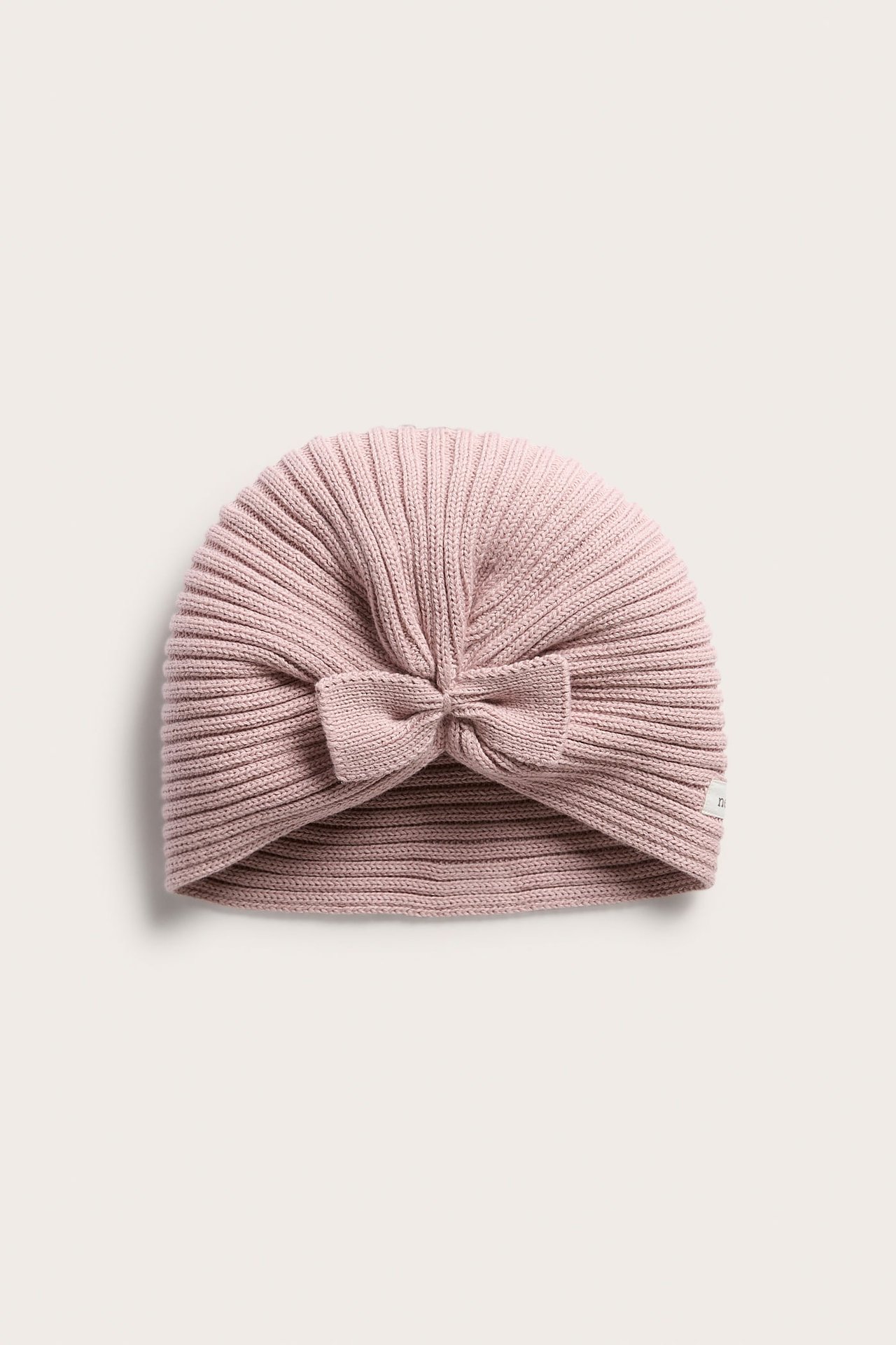 Edestä kuvattu vaaleanpunainen neulottu vauvan turbanhattu rusetilla.