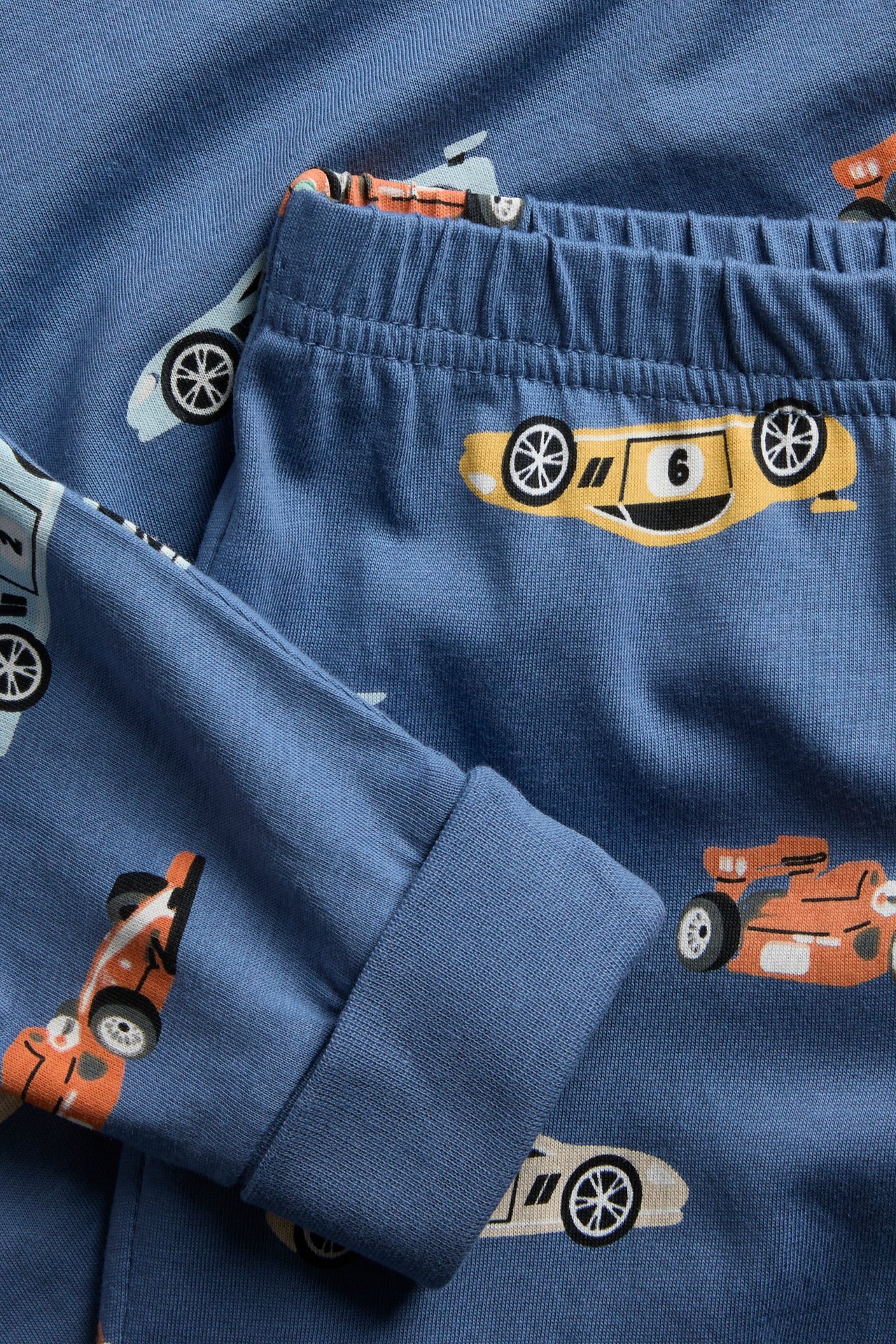 Närbild på ett blått pyjamasset för barn med resår i midjan och mönster av tecknade racerbilar.