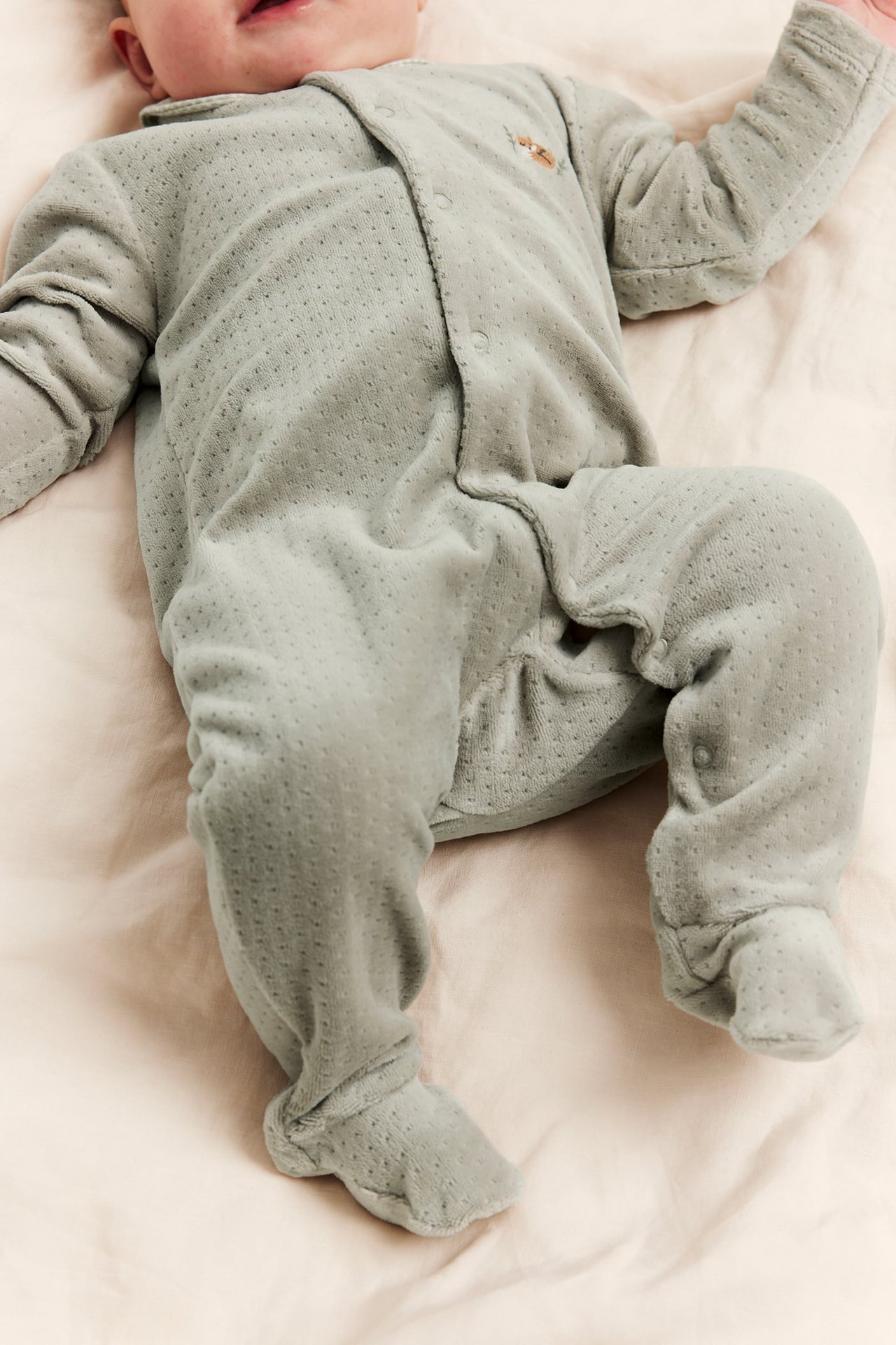 Ovenfra syn på en baby iført en lysegrønn prikket myk heldress med knapper.