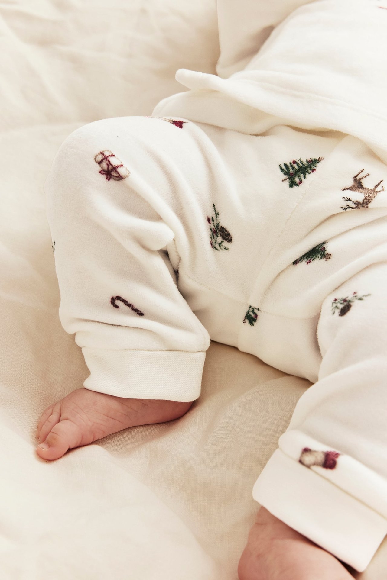 Nærbilde av baby i hvit fleecedress med broderte juletrær, reinsdyr og gaver.