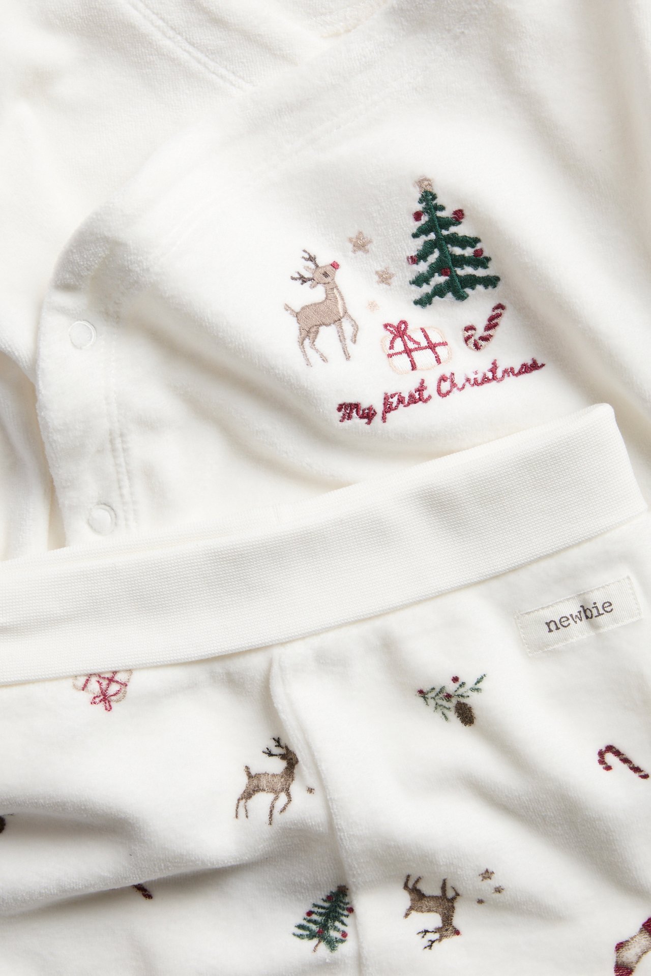 Zbliżenie miękkiego białego topu niemowlęcego z haftem 'My first Christmas' i pasującymi spodniami.