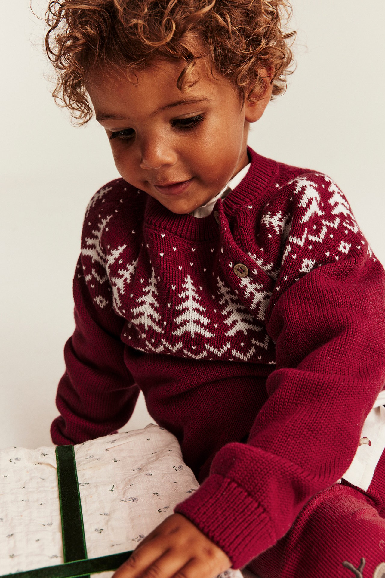 Närbild på baby i röd stickad jultröja med vita mönster och matchande byxor.