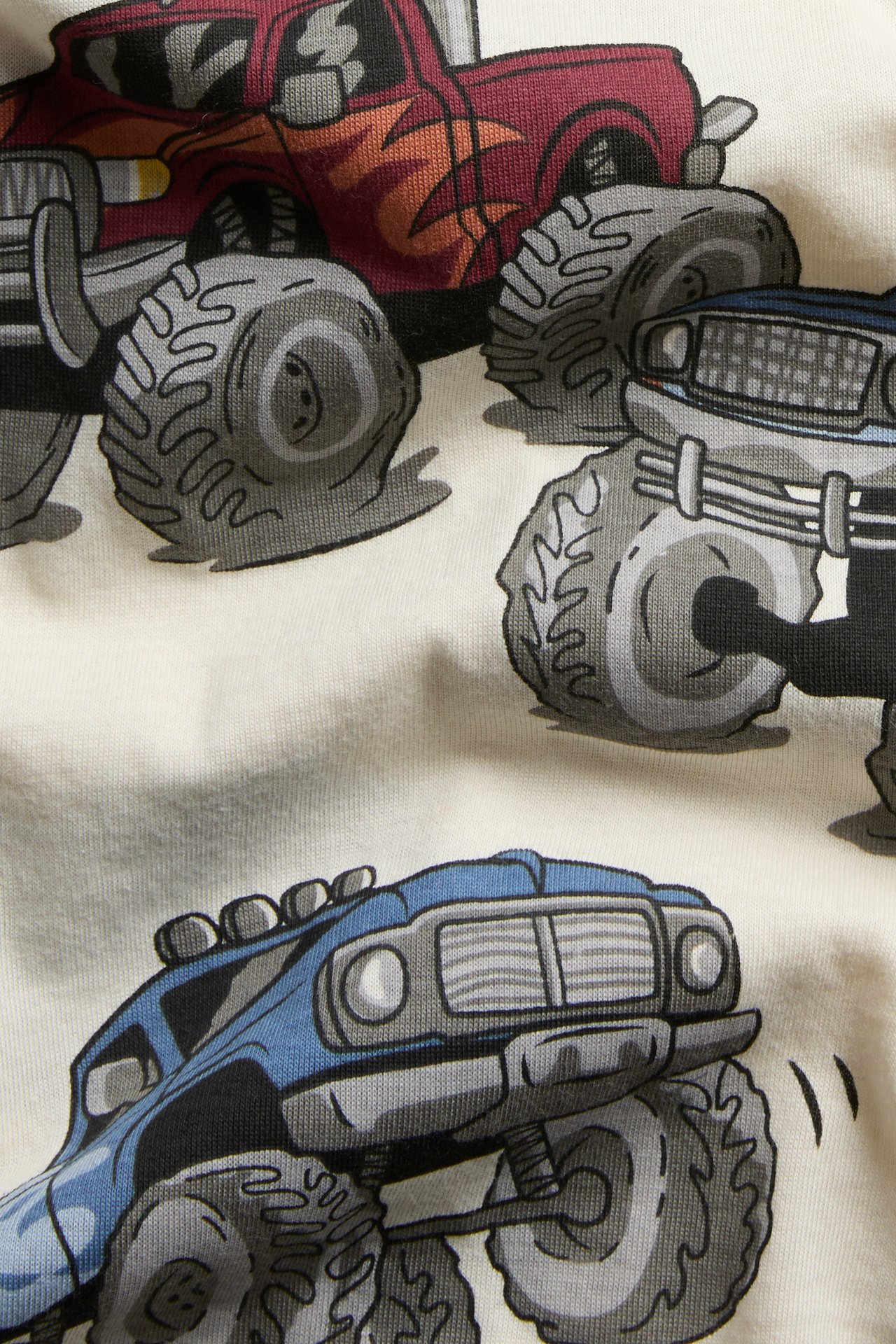 Zbliżenie kremowego materiału z czerwonym, niebieskim i szarym nadrukiem monster trucków.