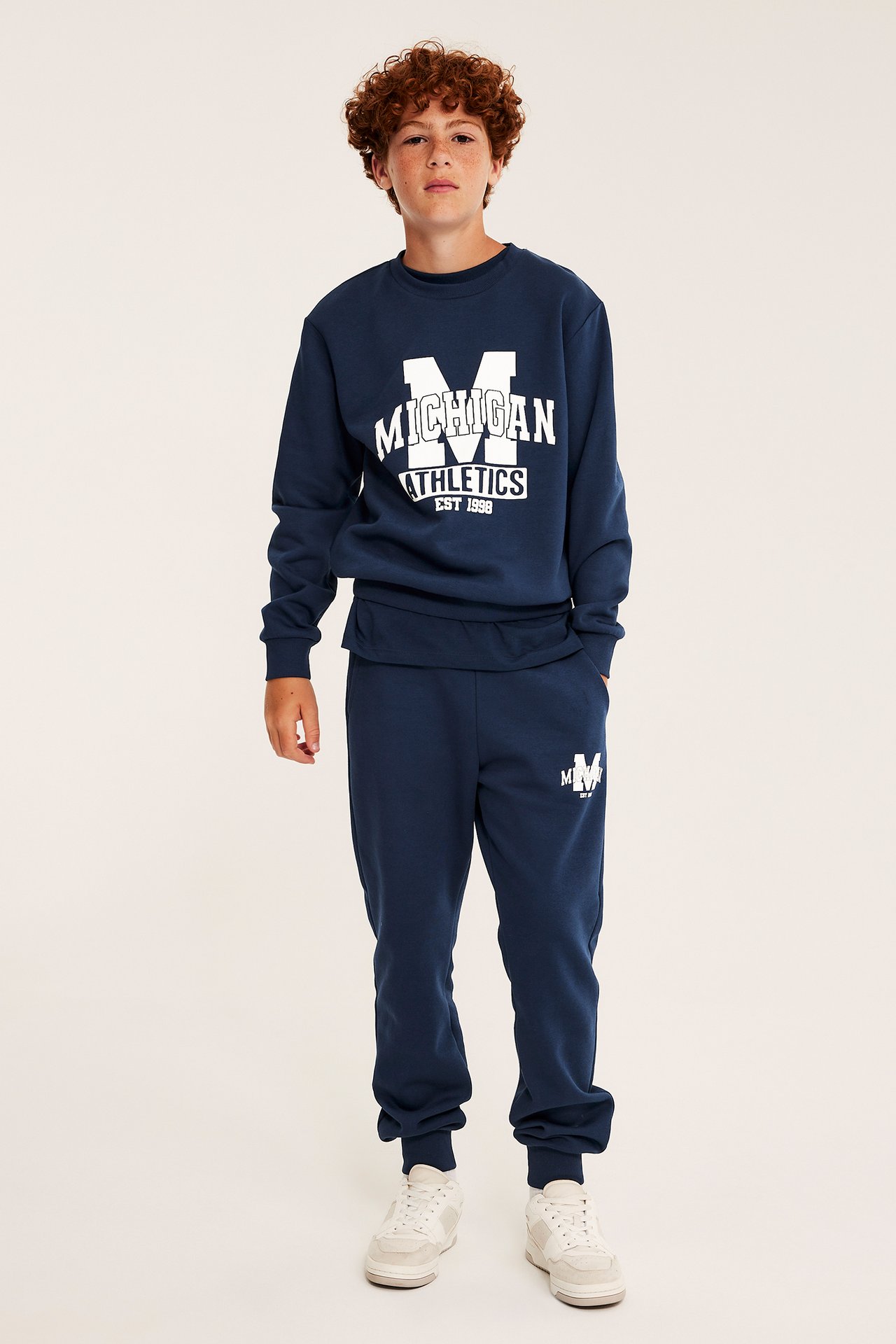 Frontbilde av barn i marineblå 'MICHIGAN ATHLETICS' genser og matchende joggebukse med hvite joggesko.