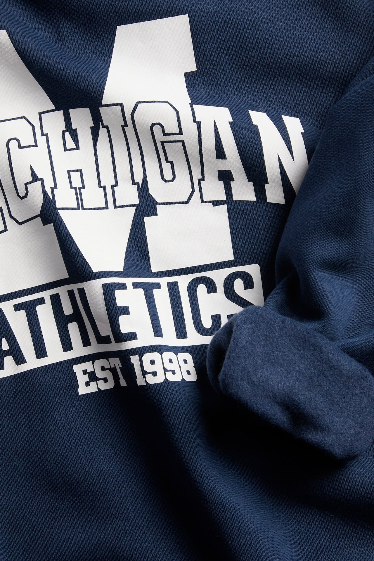 Zbliżenie na granatową bluzę z białym nadrukiem 'MICHIGAN ATHLETICS EST 1998' i podszewką z polaru.