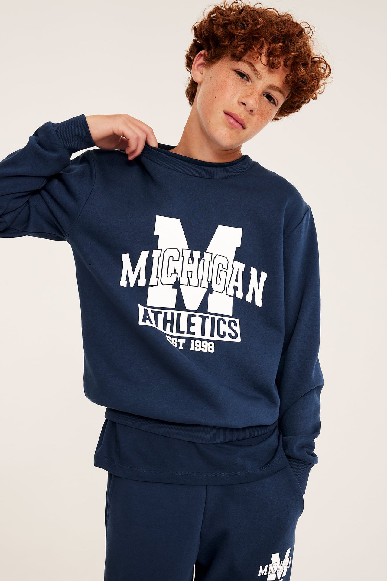 Sett forfra en gutt i mørkeblå sweatshirt med MICHIGAN ATHLETICS-trykk og matchende joggebukse.