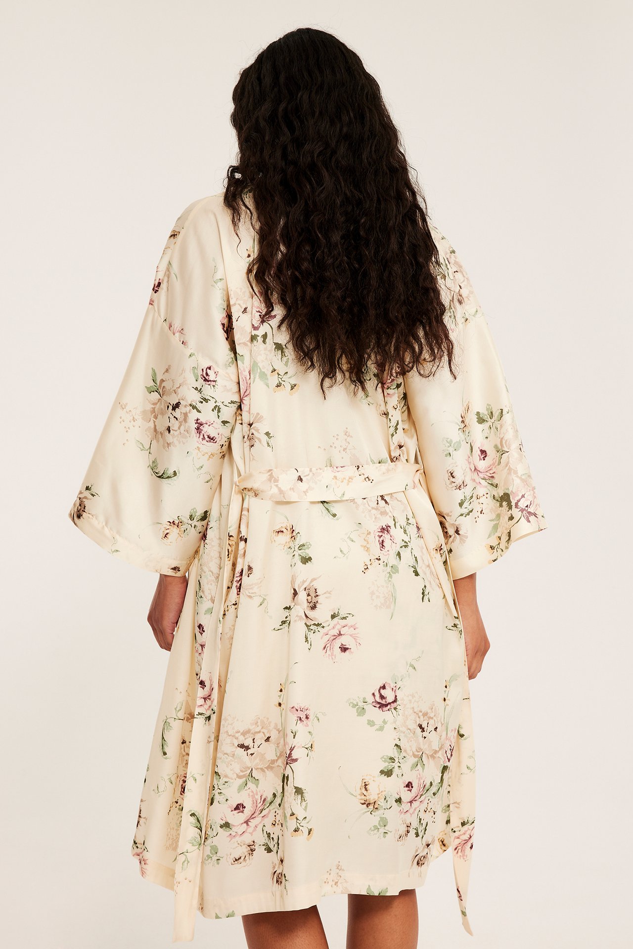 Widok z tyłu kobiety w ecru, kwiecistym satynowym szlafroku kimono z paskiem do wiązania.