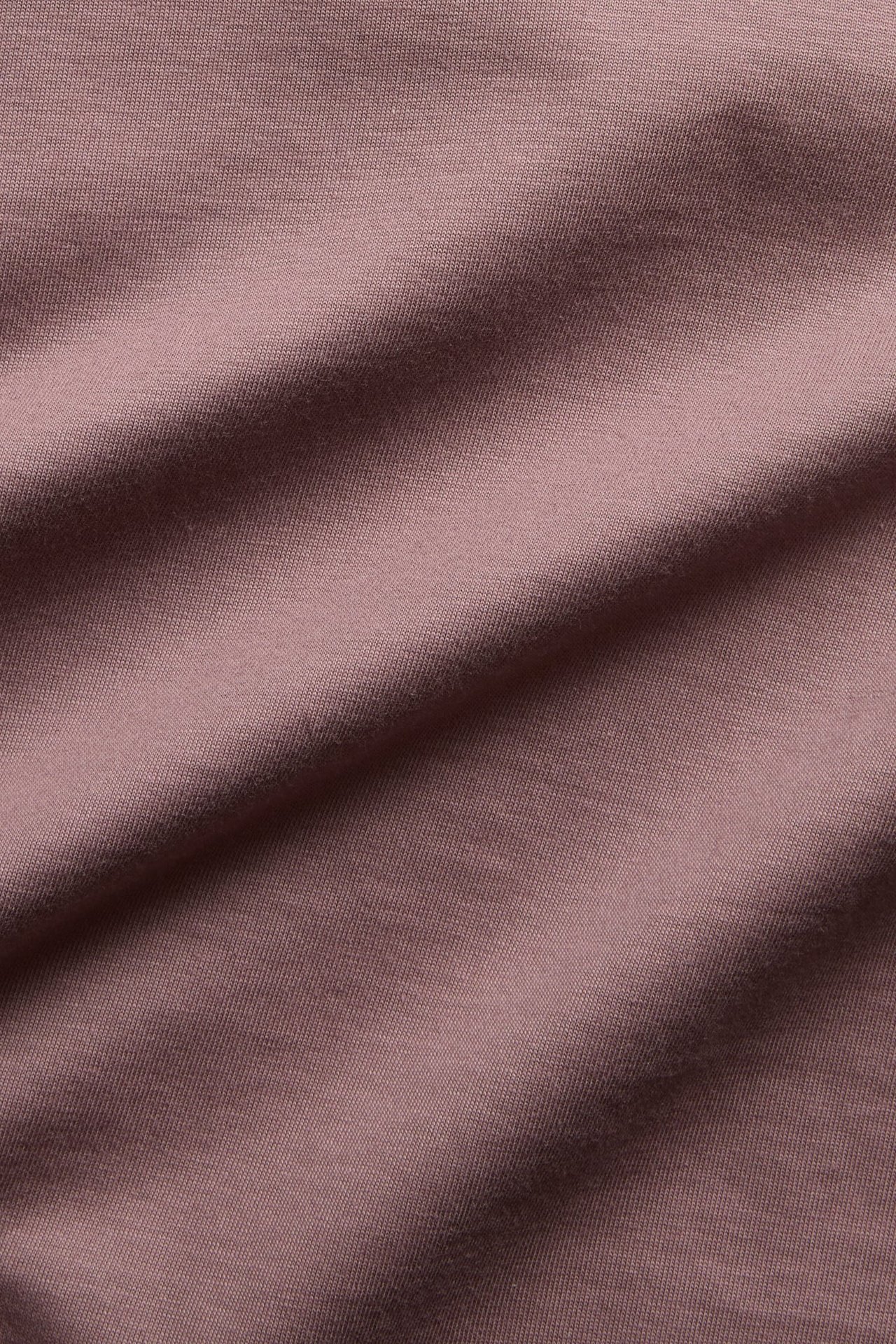 Zbliżenie na dzianinowy materiał w kolorze mauve z delikatnymi fałdami.