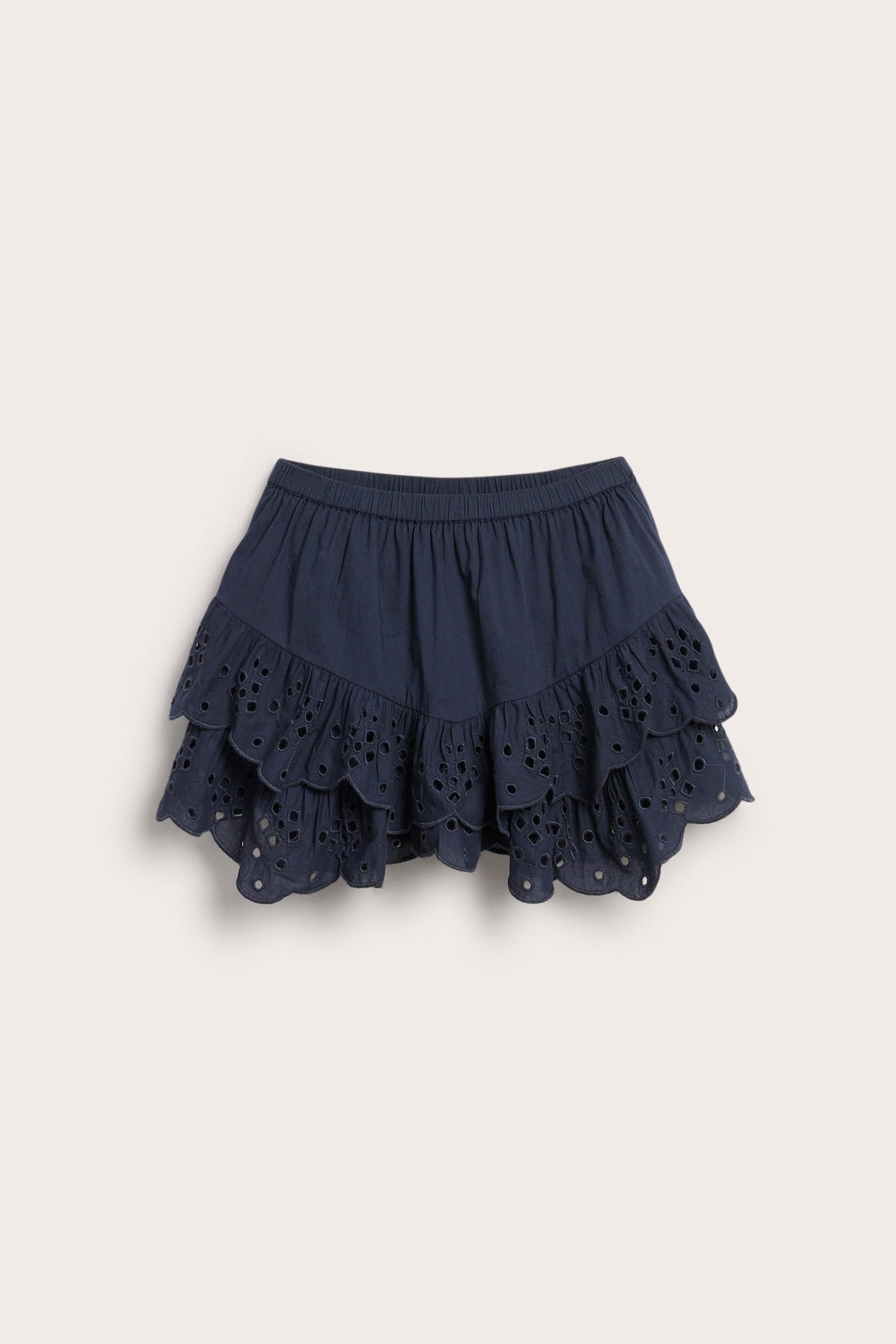 Framifrån: en mörkblå volangkjol för barn med elastisk midja och broderie anglaise på volangerna.