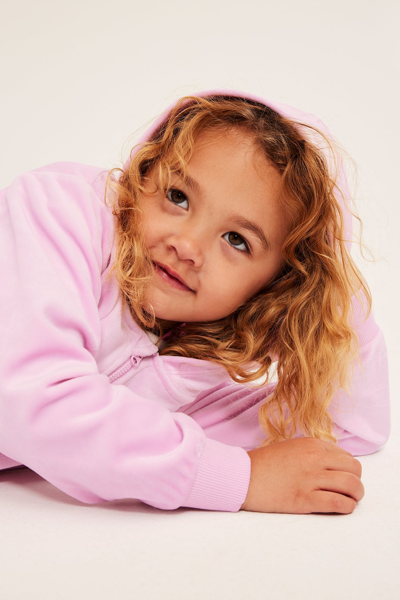 Nærbilde, vinklet visning av et barn som har på seg en rosa velour hoodie med full glidelås.