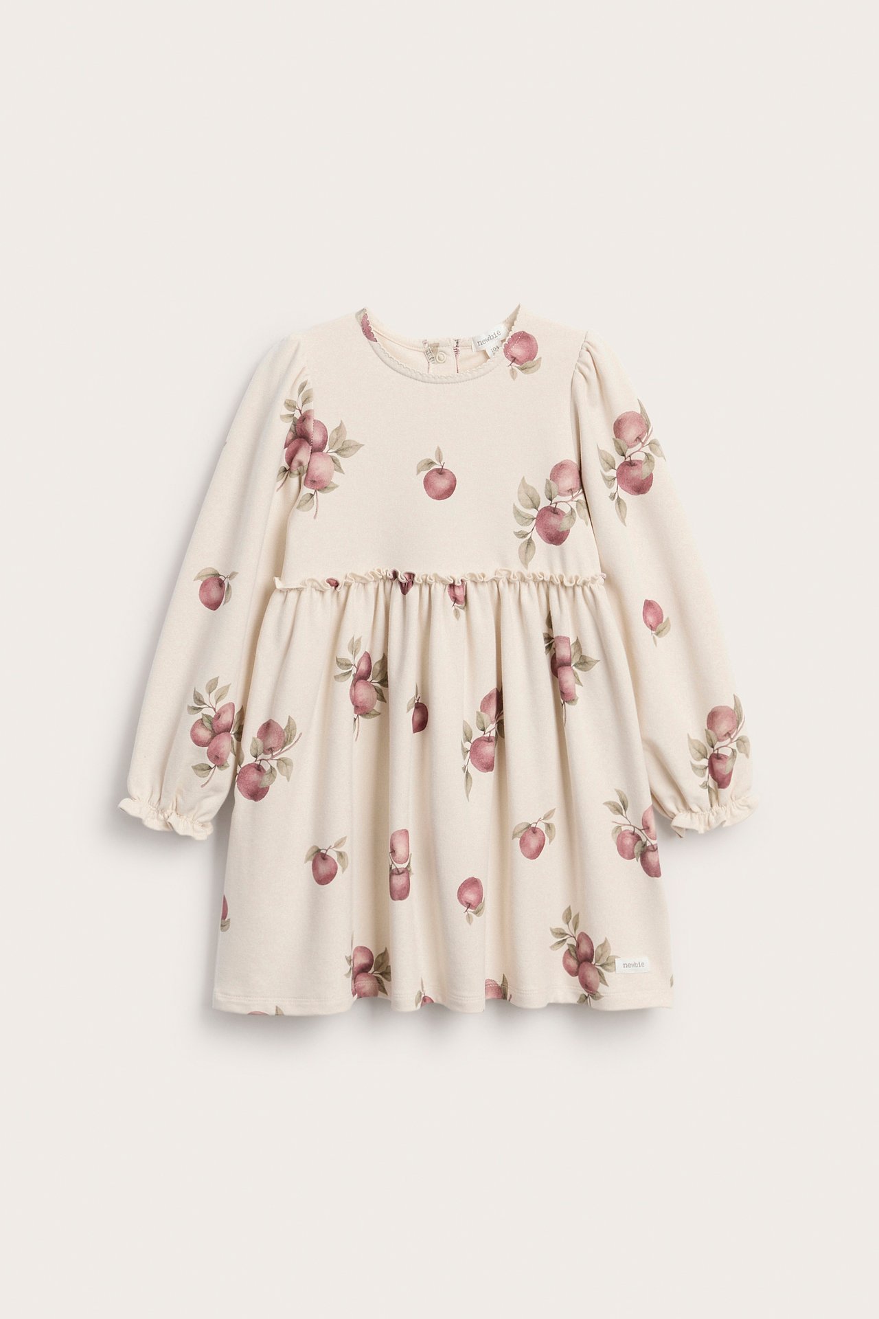 Framifrån, en beige babyklänning med rött äppeltryck, långa volangärmar och samlad kjol.