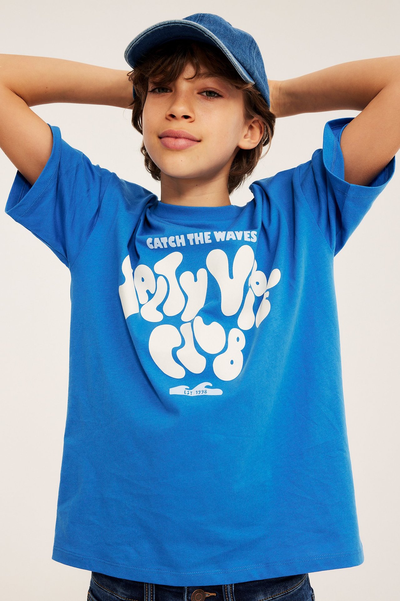 Z przodu: Dziecko w niebieskim T-shircie z białym nadrukiem i niebieskiej dżinsowej czapce.