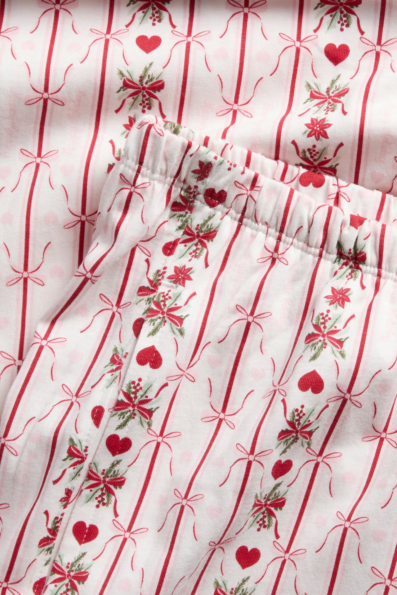 Närbild på vita pyjamasbyxor med rött julrandigt, rosett-, hjärt- och järnekmönster.