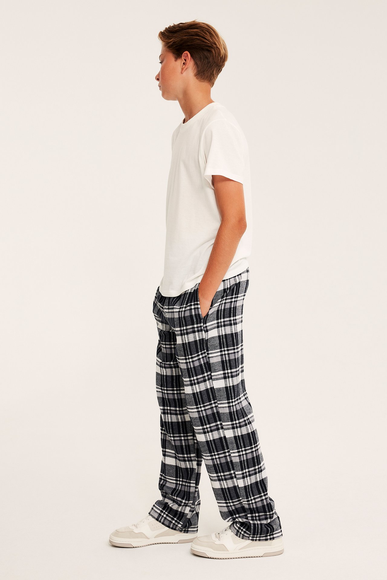 Sidovy av barn i svartvitrutiga pyjamasbyxor, en vit t-shirt och vita sneakers.
