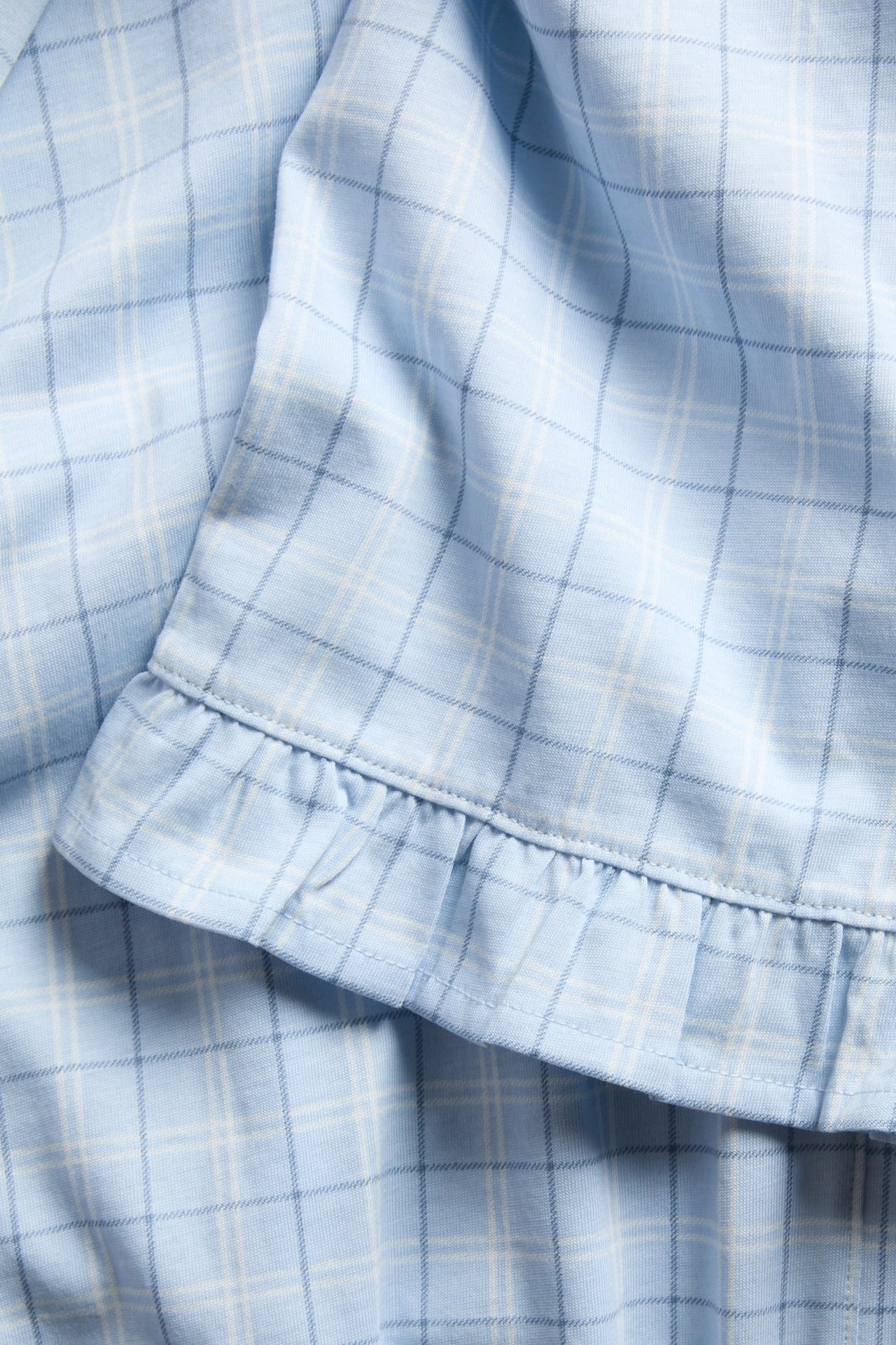 Lähikuva vaaleansinisistä ruudullisista jersey-pyjamahousuista, joissa on röyhelöreuna.