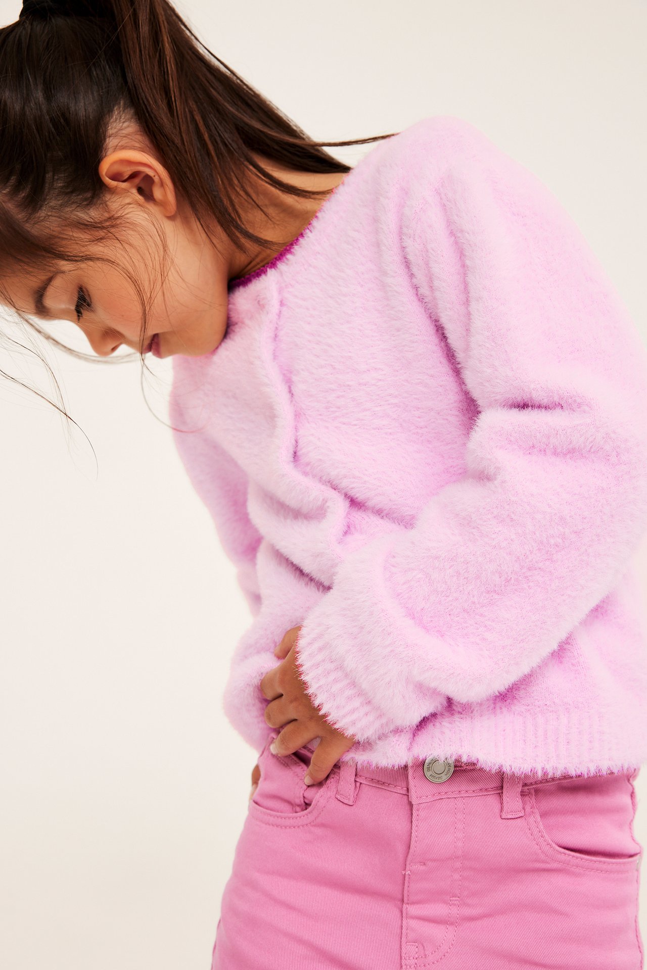 Sideutsnitt av et barn i rosa fluffy genser med ribbet kant og rosa jeans.