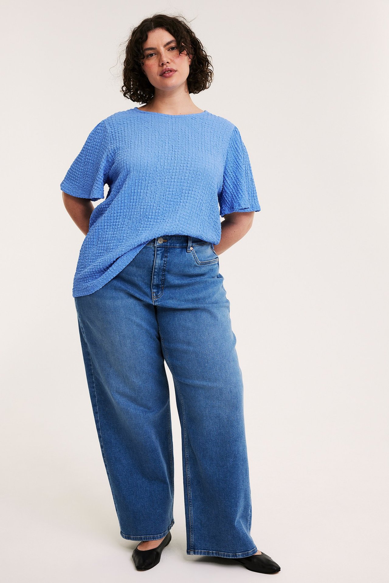 Widok z przodu: kobieta w niebieskim, teksturowanym topie, szerokich jeansach, czarnych baletkach.