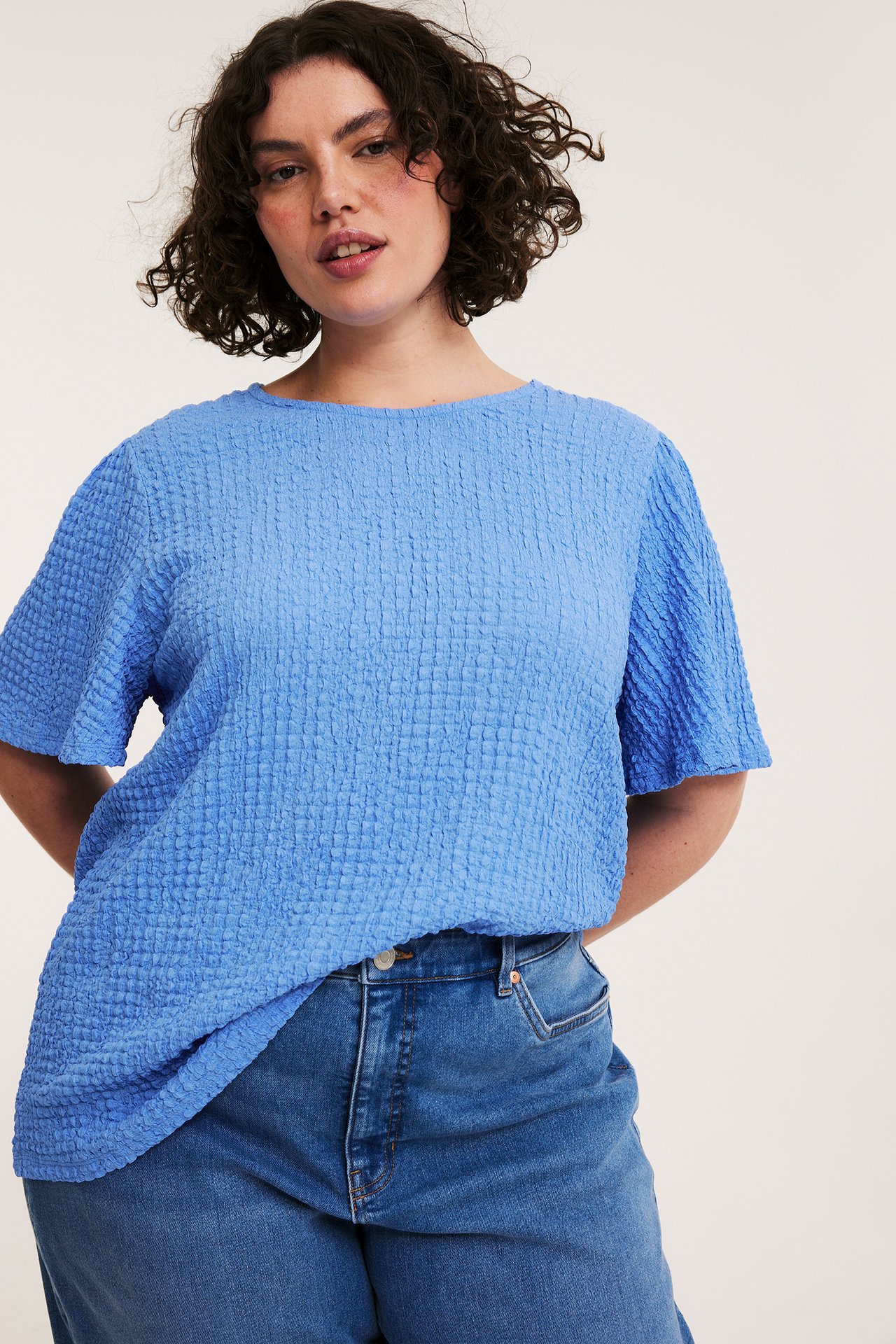 Edestä, nainen yllään löysä sininen teksturoitu lyhythihainen toppi ja siniset farkut.