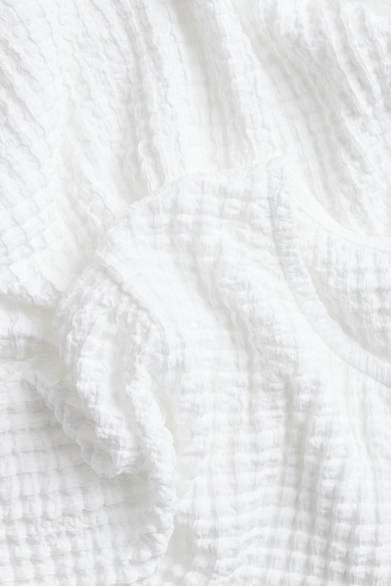 Lähikuva valkoisesta lyhythihaisesta topista, jossa on kuvioitu, ryppyinen pinta.