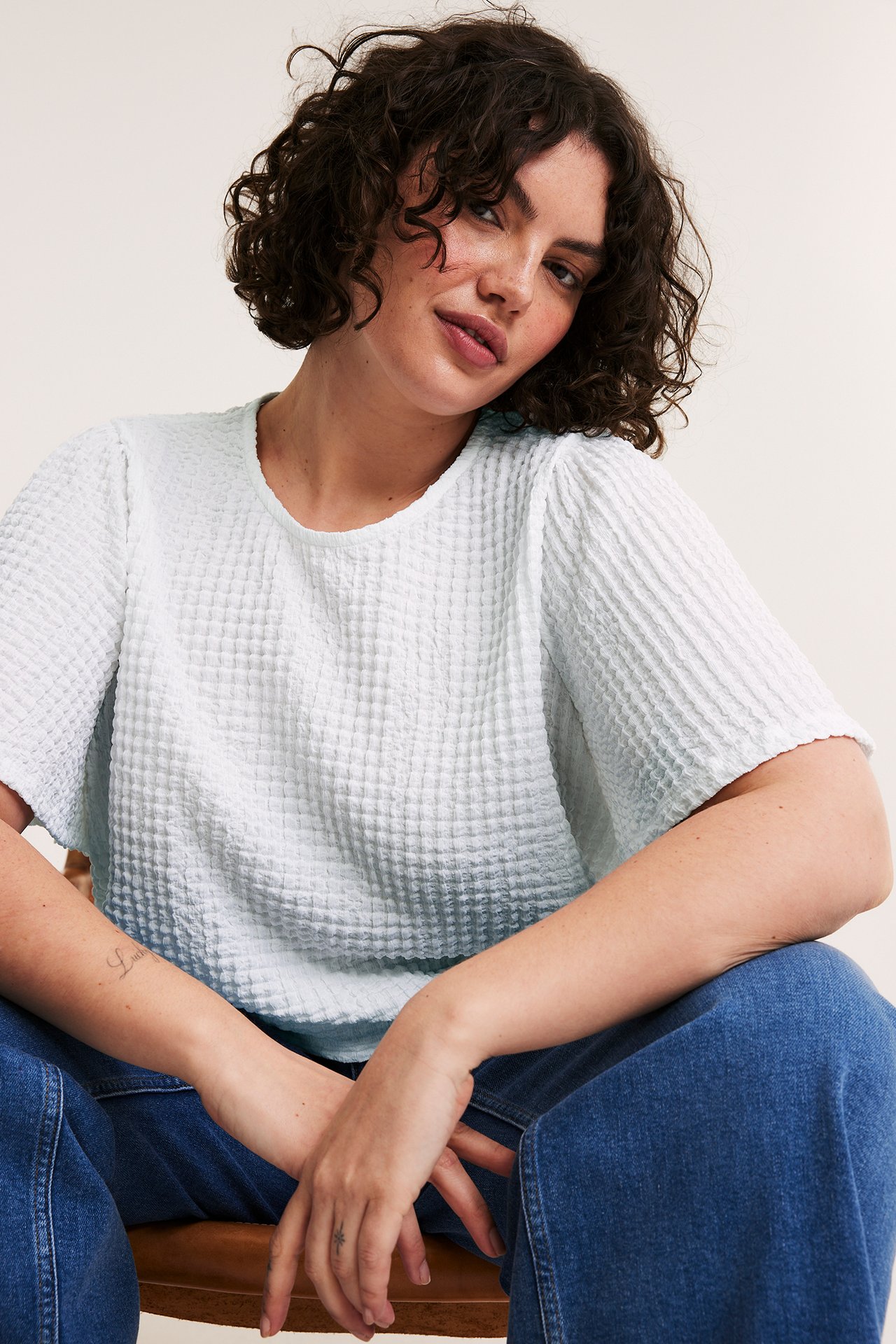 Edestä: nainen valkoisessa strukturoidussa lyhythihaisessa topissa ja sinisissä leveissä farkuissa.