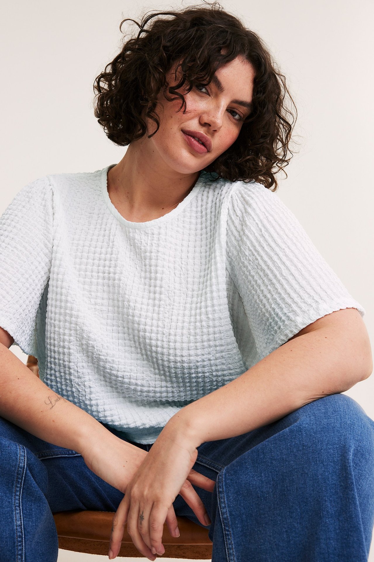 Przód: kobieta w białym, strukturalnym, krótkim topie i niebieskich szerokich dżinsach.