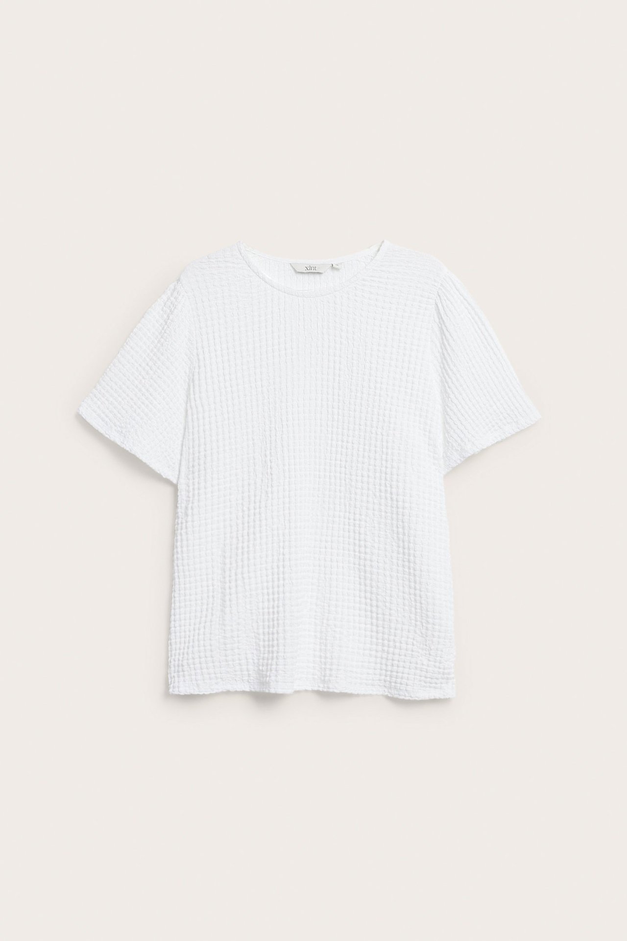 Widok z przodu białego, luźnego, krótkiego topu z teksturowanej tkaniny z okrągłym dekoltem.
