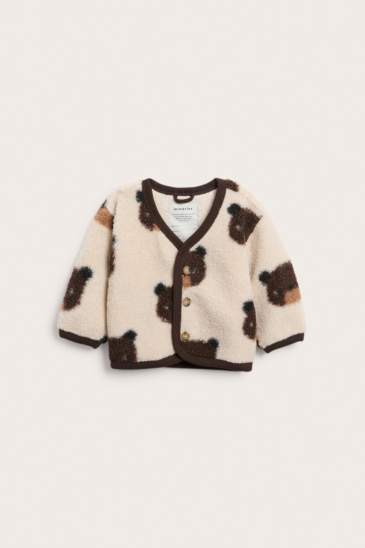 Edestä vauvan kermanvärinen fleece-neuletakki, jossa ruskeita karhunpäitä ja kaksi ruskeaa nappia.