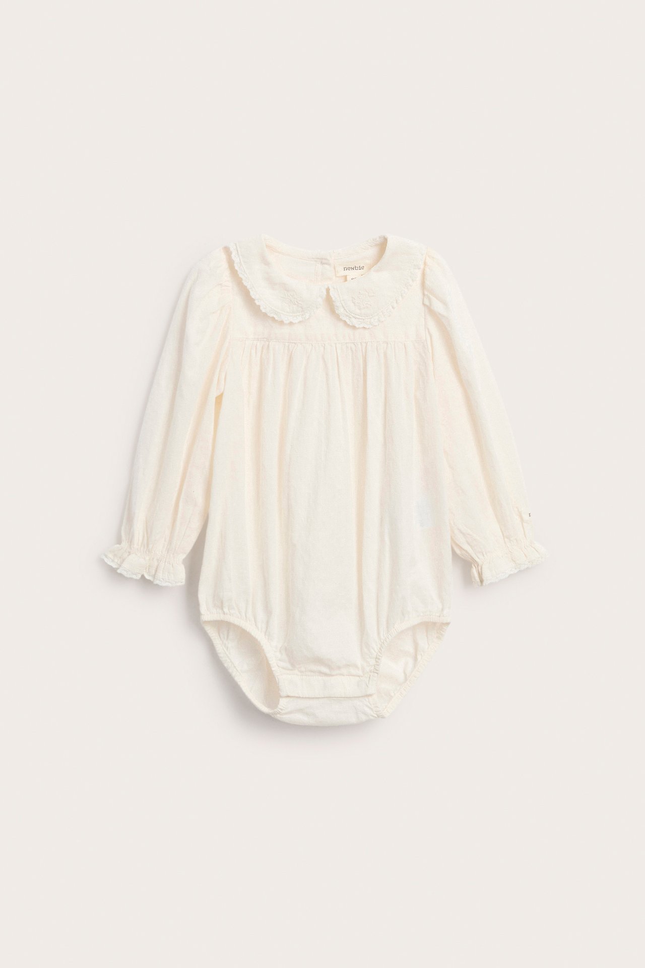 Front, kremfarget baby sparkedrakt med lange ermer, brodert krage og rysjekanter.