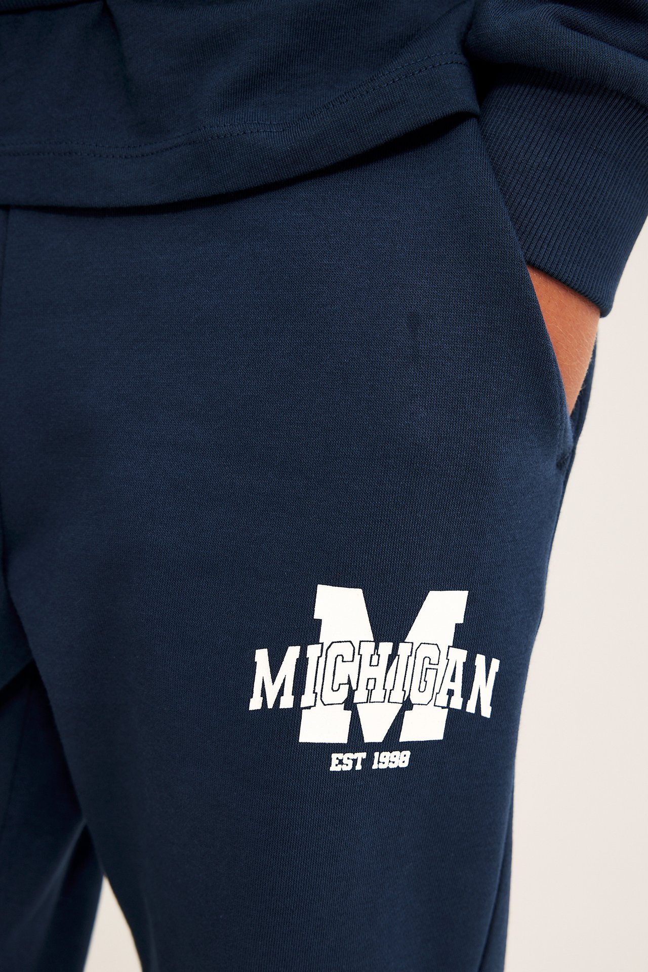 Zbliżenie na granatowe spodnie dresowe z białym logo 'MICHIGAN EST 1998', noszone z granatową bluzką.