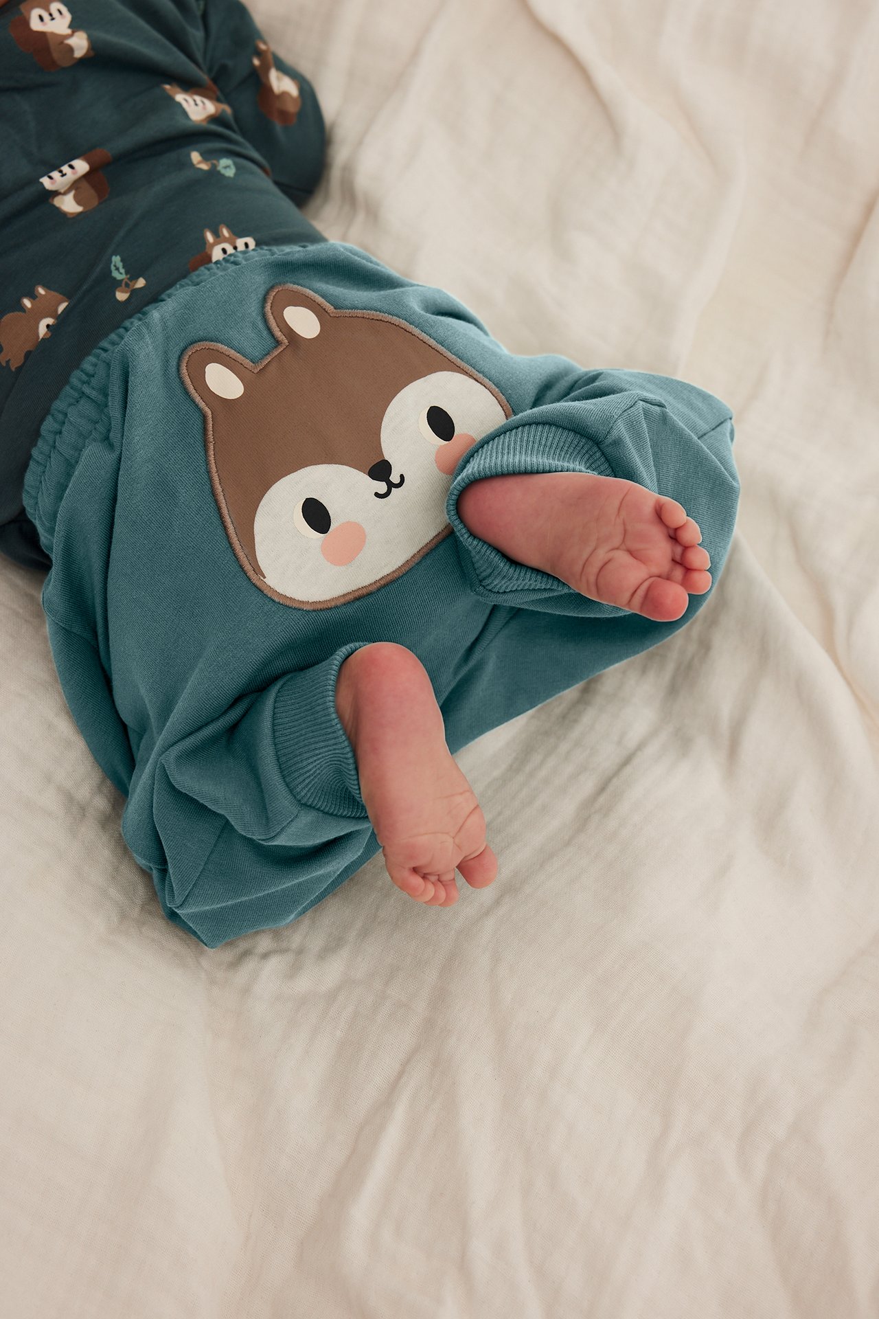 Ovanifrån: Baby i teal byxor med ekorreapplikation och mörk teal topp med ekorrmönster.