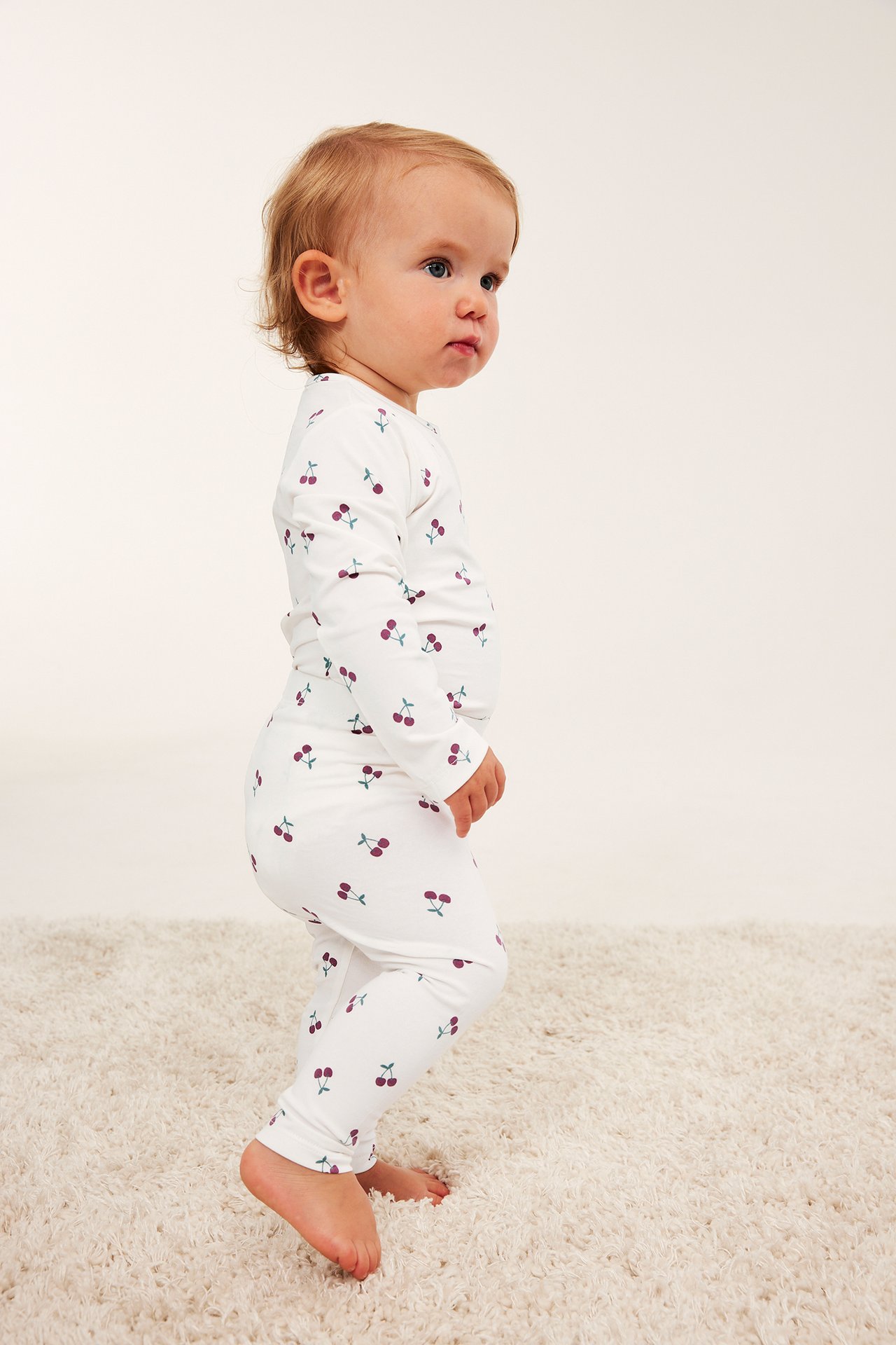 Sidovy av baby i vit körsbärsmönstrad långärmad pyjamas.